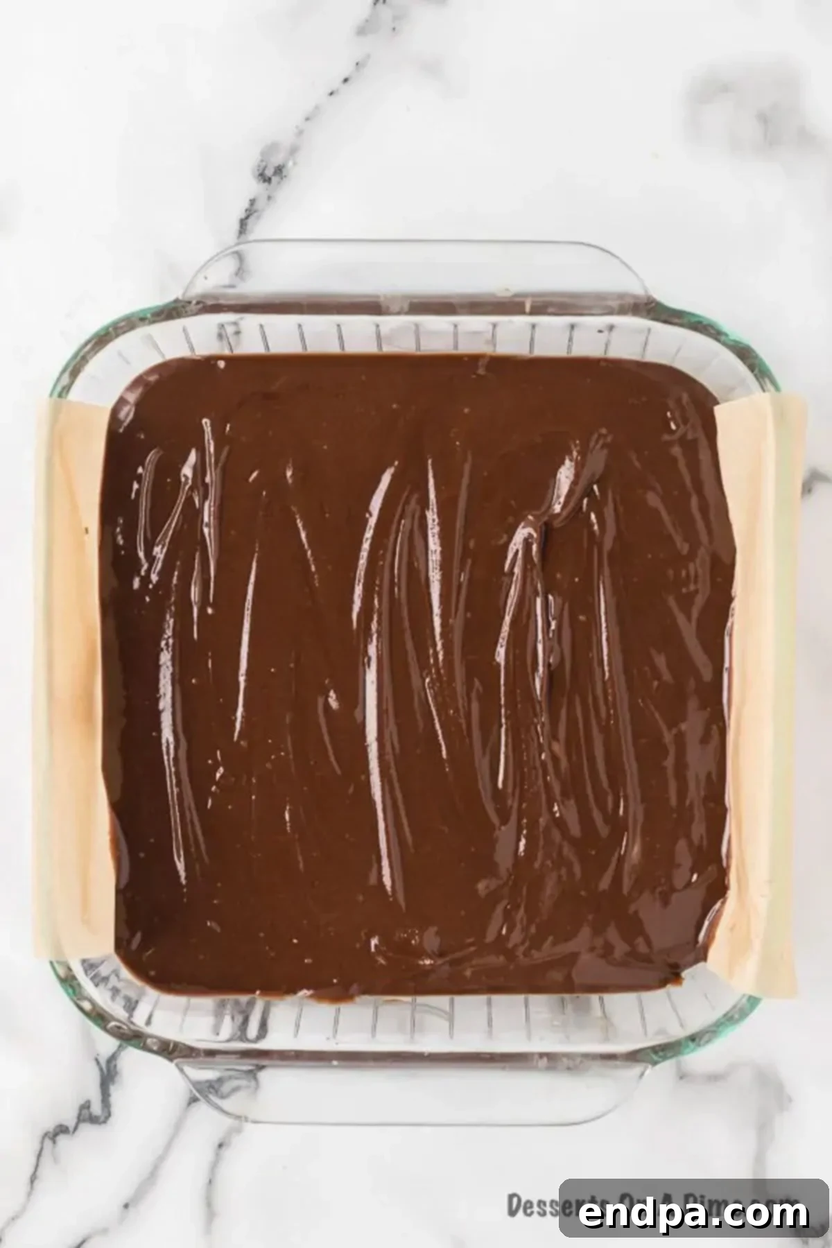 Chocolate peanut butter fudge mixture evenly spread in a baking pan lined with parchment paper, starting to cool.