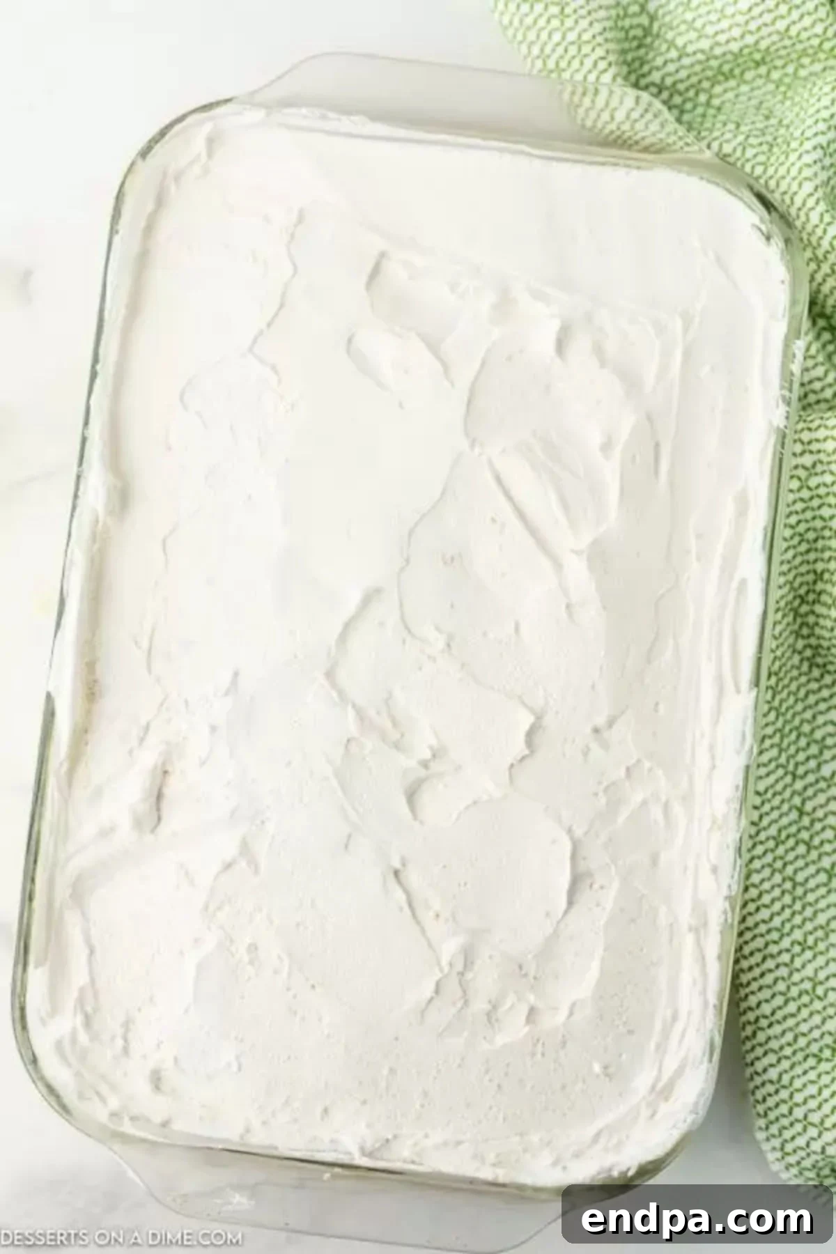 Remaining Cool Whip being spread smoothly over the creamy dirt cake layer in the baking dish.