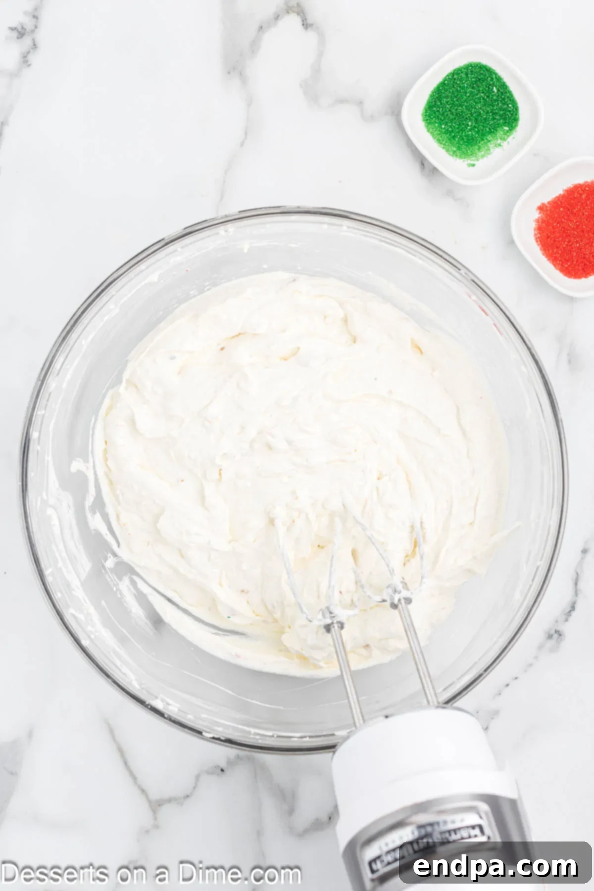 The dip mixture, now thoroughly combined and creamy, in a mixing bowl after being blended with a hand mixer, showing the flecks of Christmas tree cake.