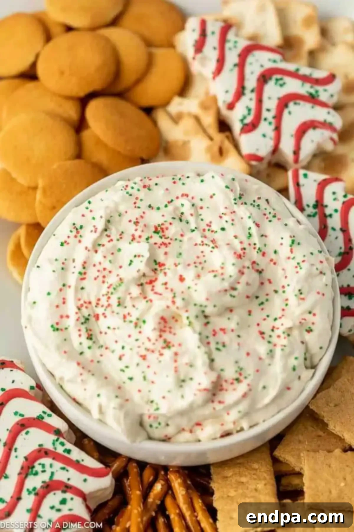 A vibrant display of Little Debbie Christmas Tree Dip in a bowl, surrounded by an inviting assortment of dippers, including pretzels, cookies, and fruit, ready for a festive gathering.