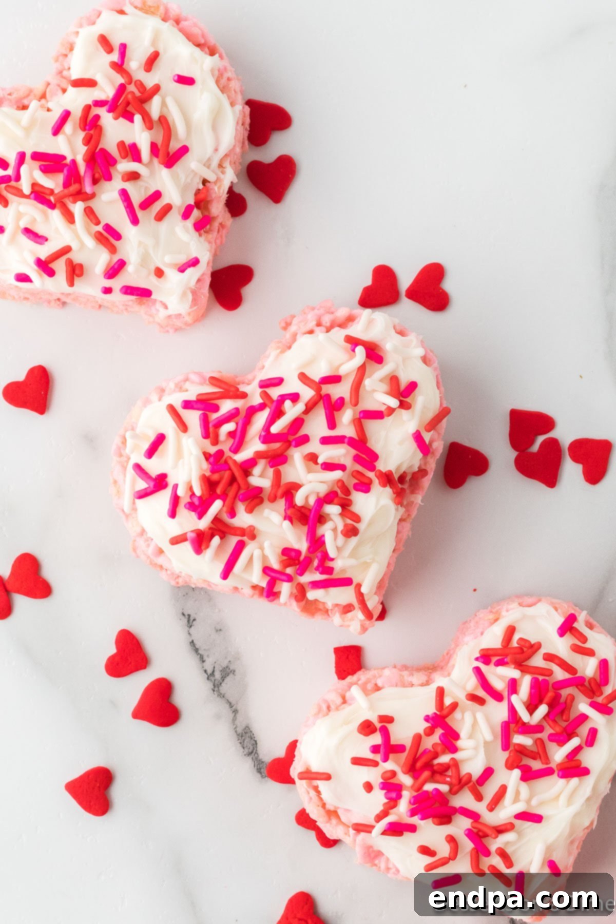 Sweetheart Crispy Treats 2 Valentine Rice Krispie Treats surrounded by little hearts. These treats are heart-shaped and topped with pink frosting and festive sprinkles, perfect for Valentine's Day.
