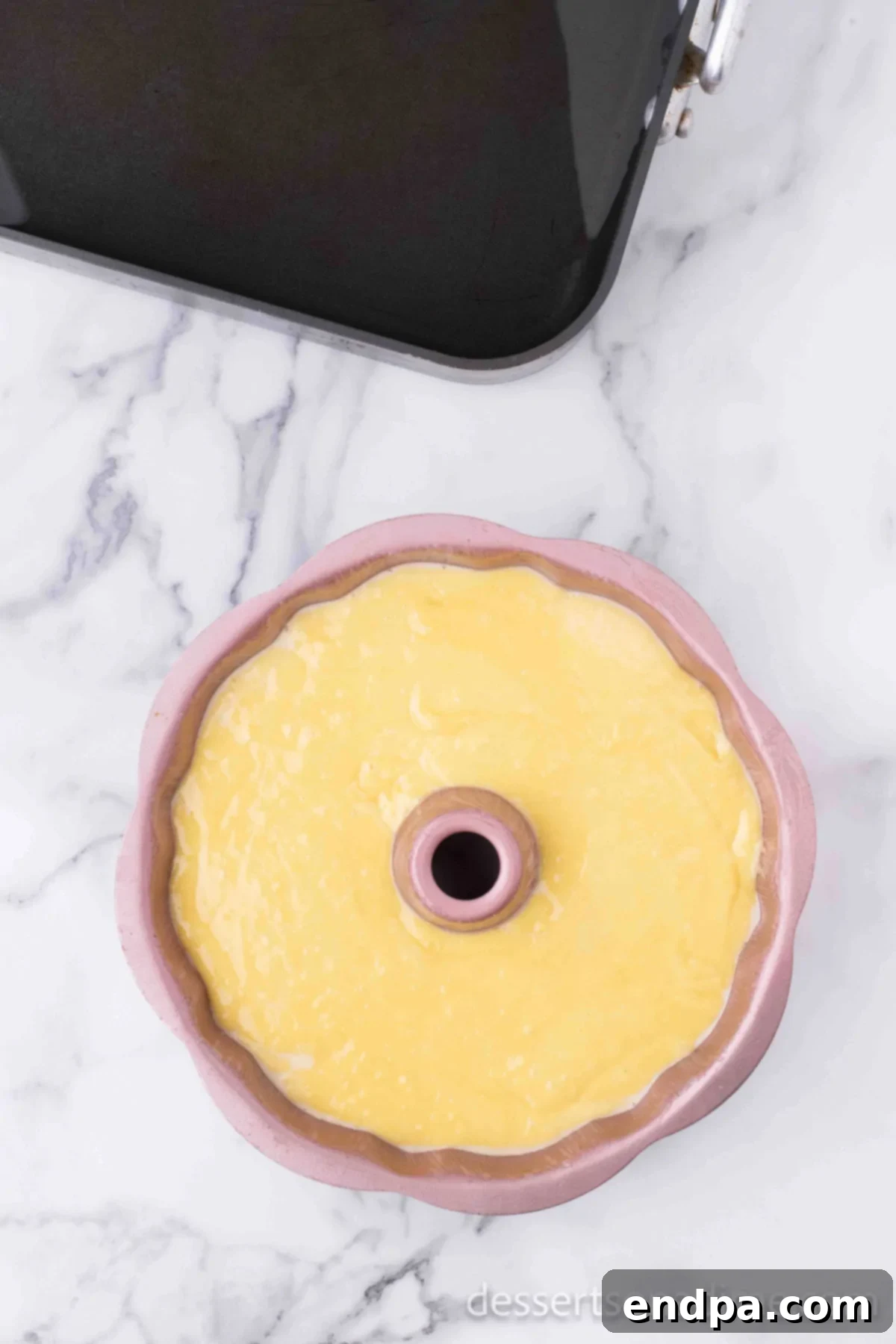 Cake batter being poured on top of the flan mixture in the bundt pan.