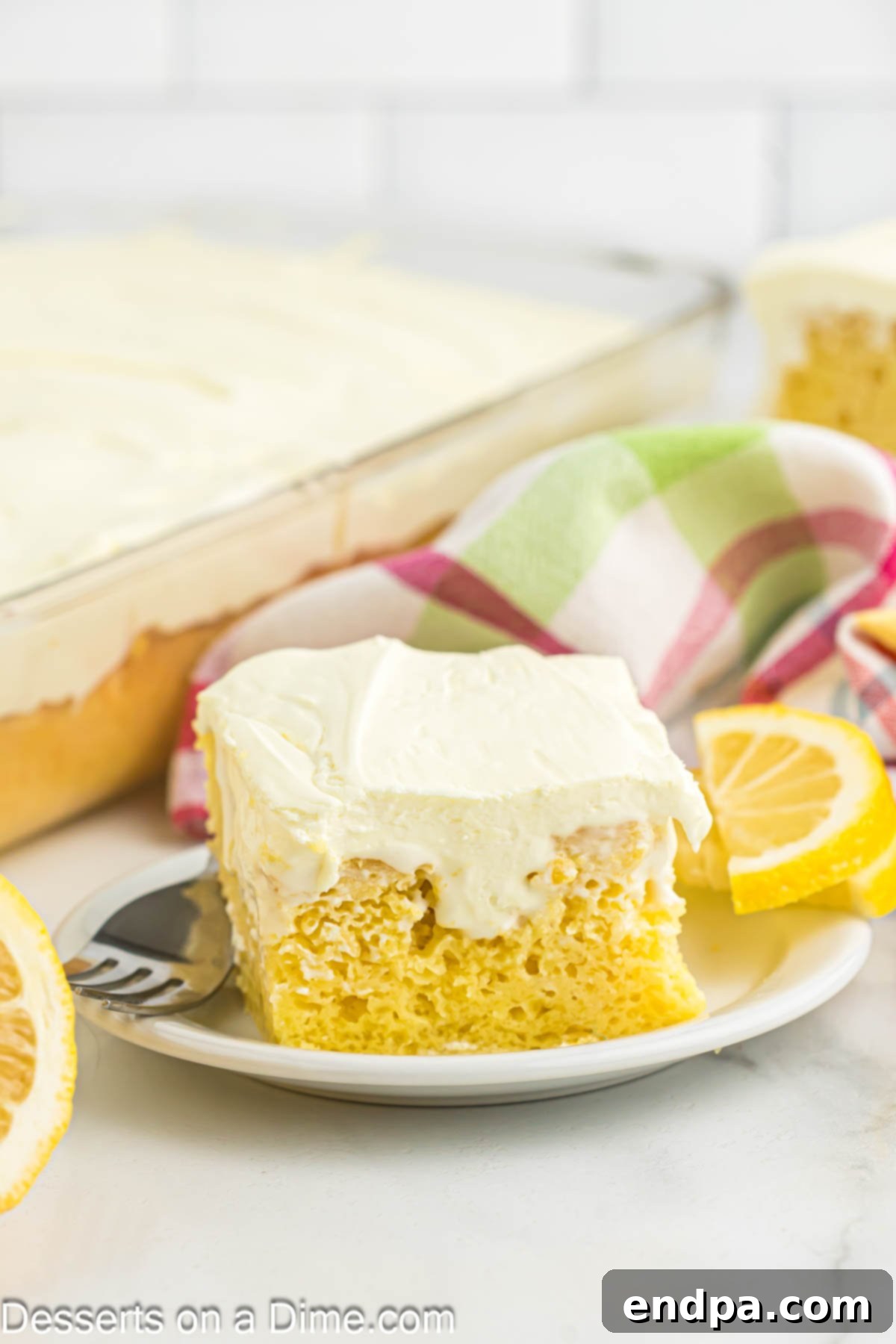 A slice of Lemon Poke Cake on a white plate, topped with whipped cream and lemon zest.