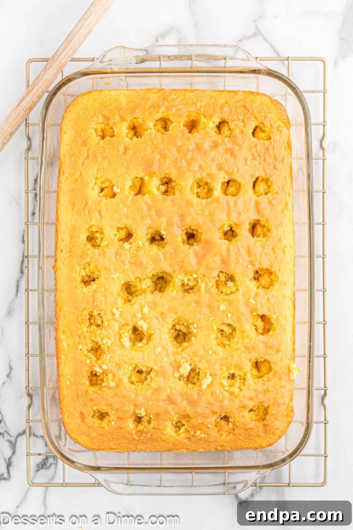Holes being poked into the warm lemon cake with the handle of a wooden spoon.