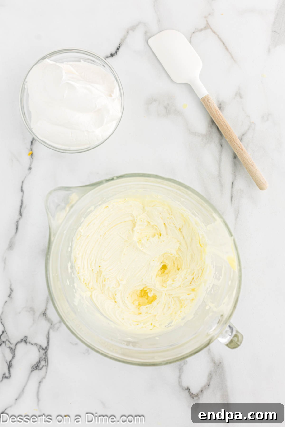 Lemon frosting being beaten in a mixing bowl with a hand mixer.