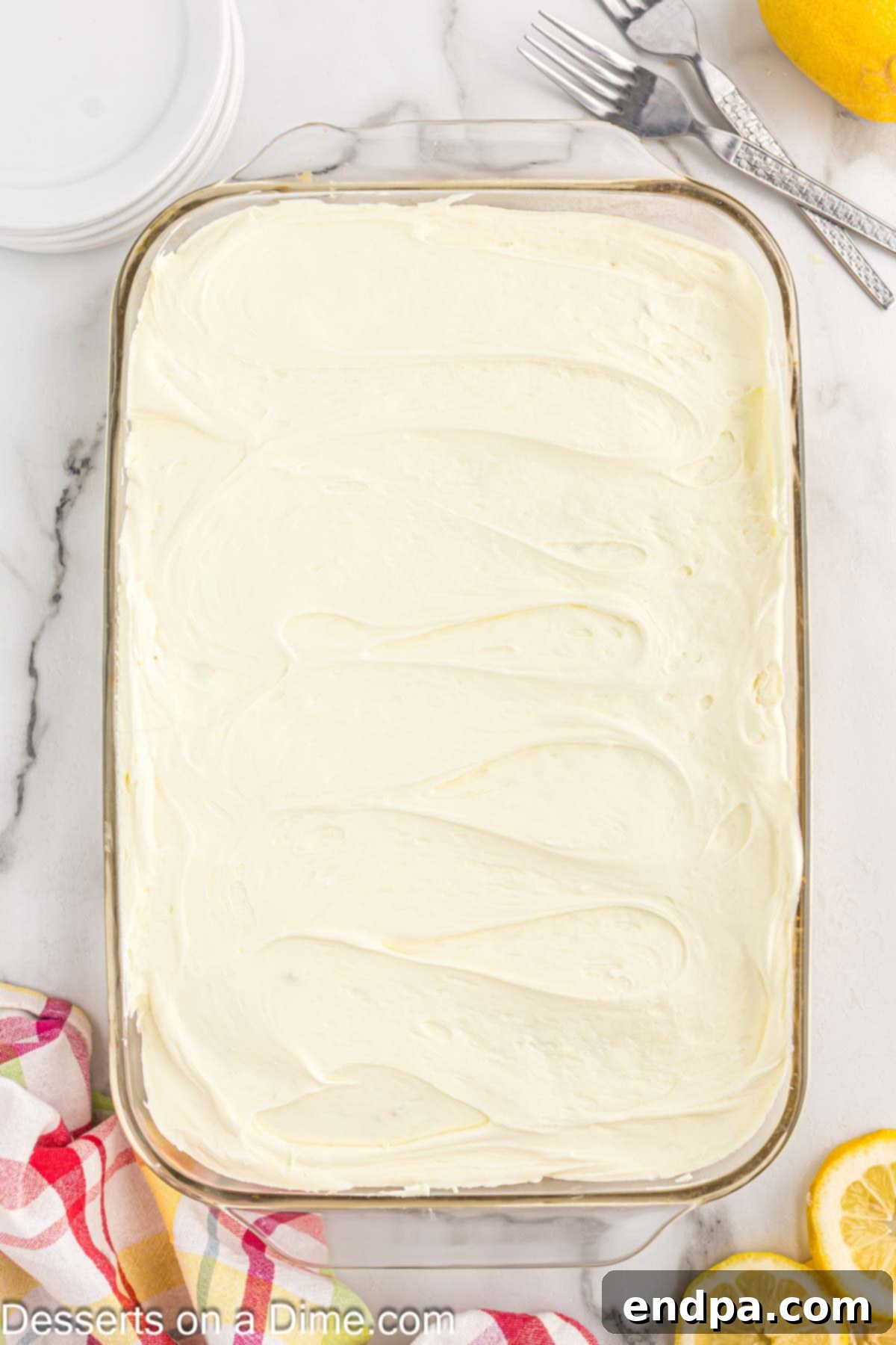 The prepared lemon whipped frosting being spread evenly over the chilled lemon poke cake.