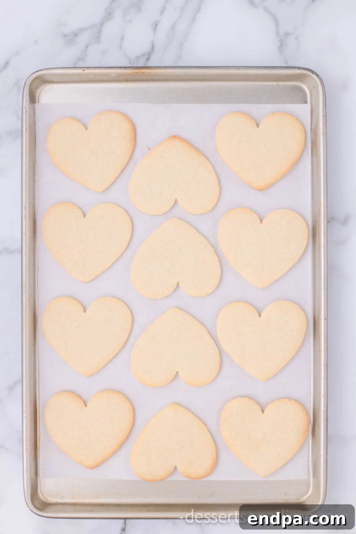 Baked heart-shaped cookies, lightly golden brown around the edges, resting on a wire rack to cool completely.