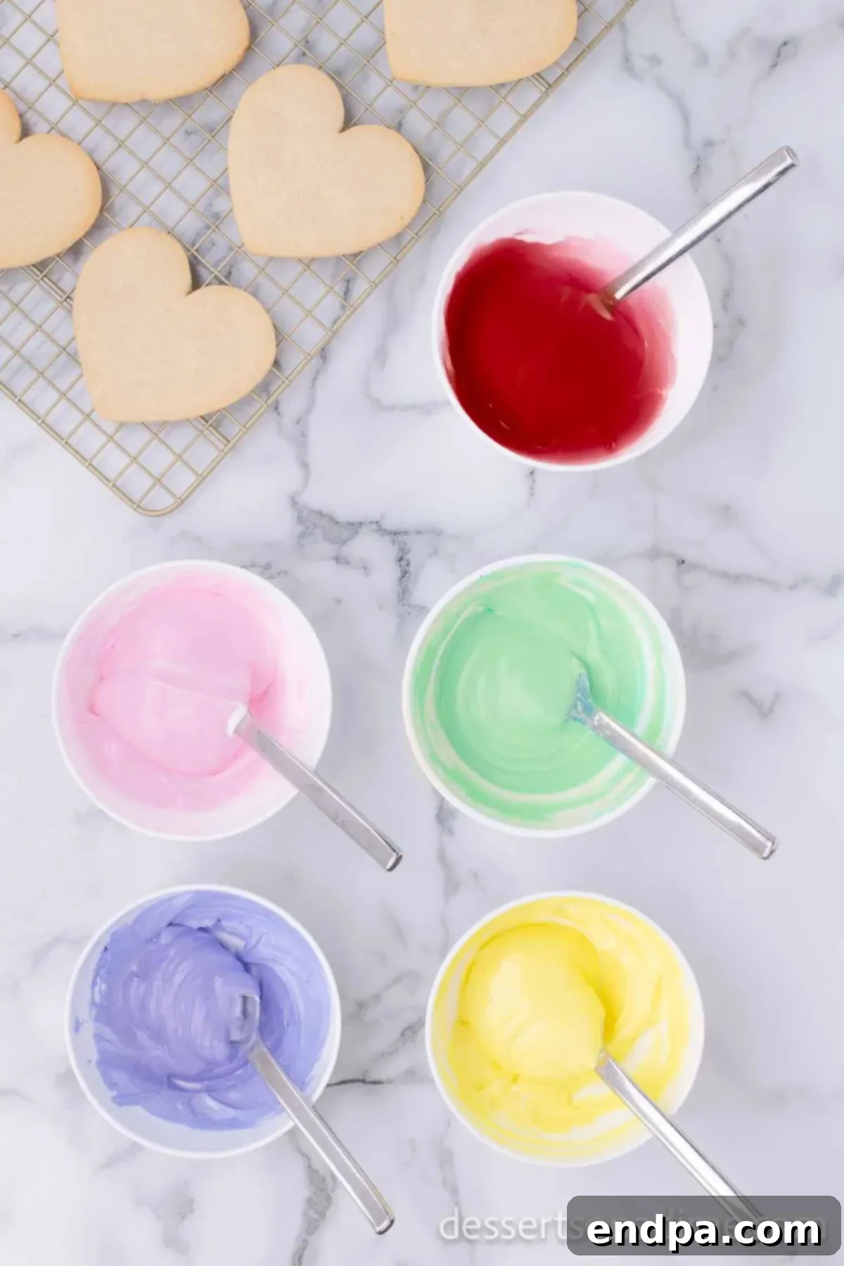 Several small bowls of royal icing, each tinted with a different pastel food coloring, ready for decorating.