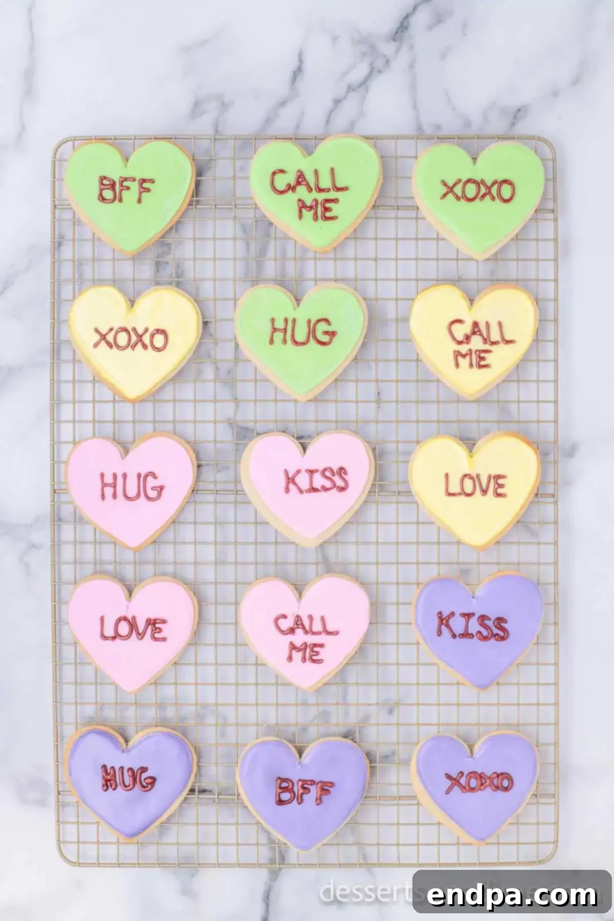 A selection of decorated heart-shaped sugar cookies with various pastel icings and handwritten Valentine's messages, displayed on a wire rack.