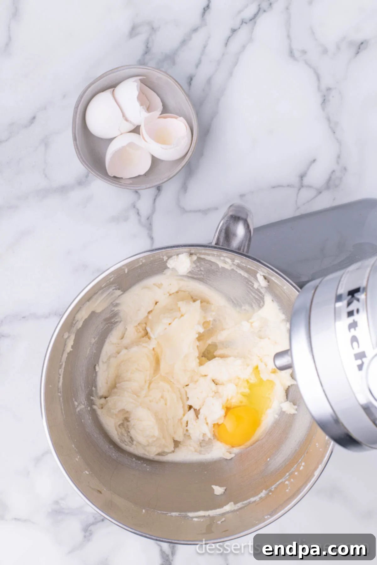 Cracked eggs being added one by one to the creamed butter and sugar mixture in a mixing bowl.