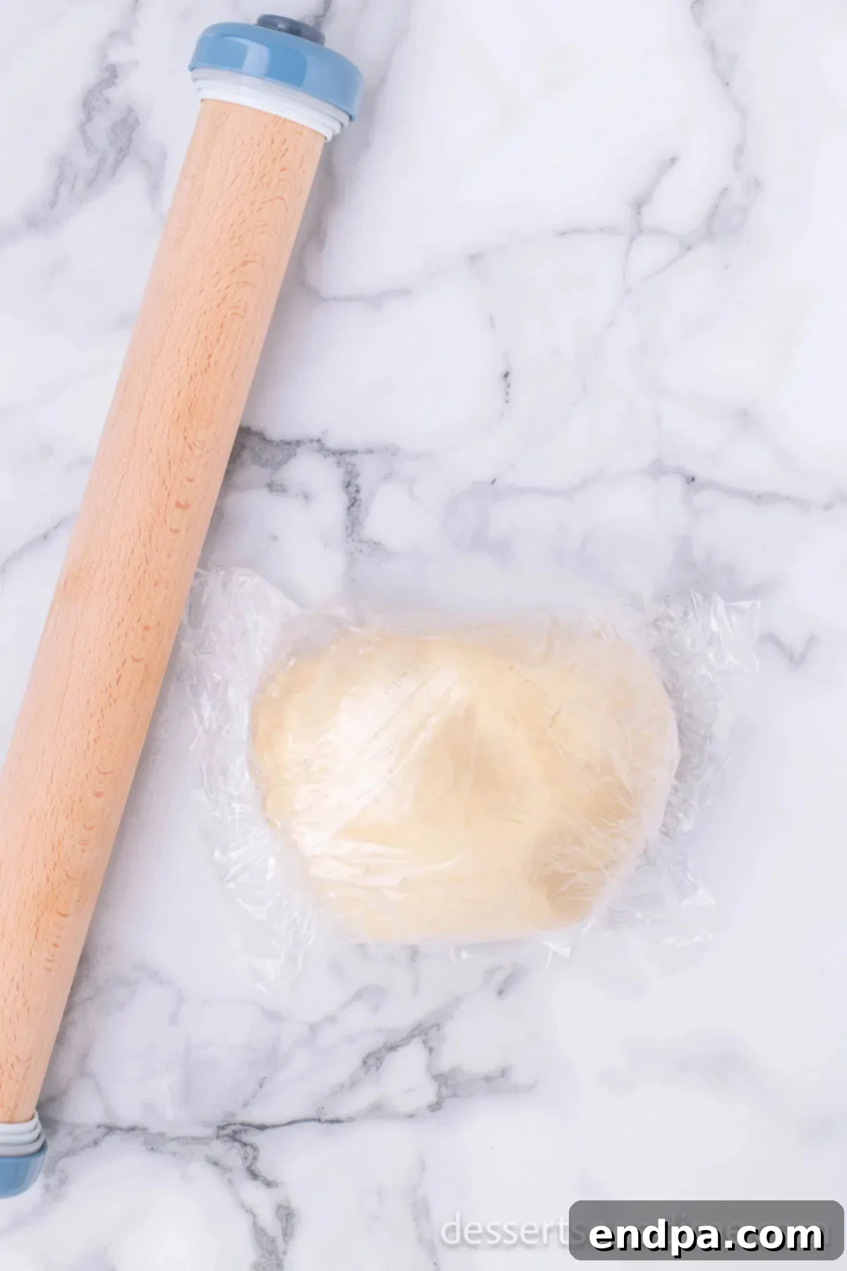 A ball of sugar cookie dough tightly wrapped in plastic wrap, indicating preparation for chilling.