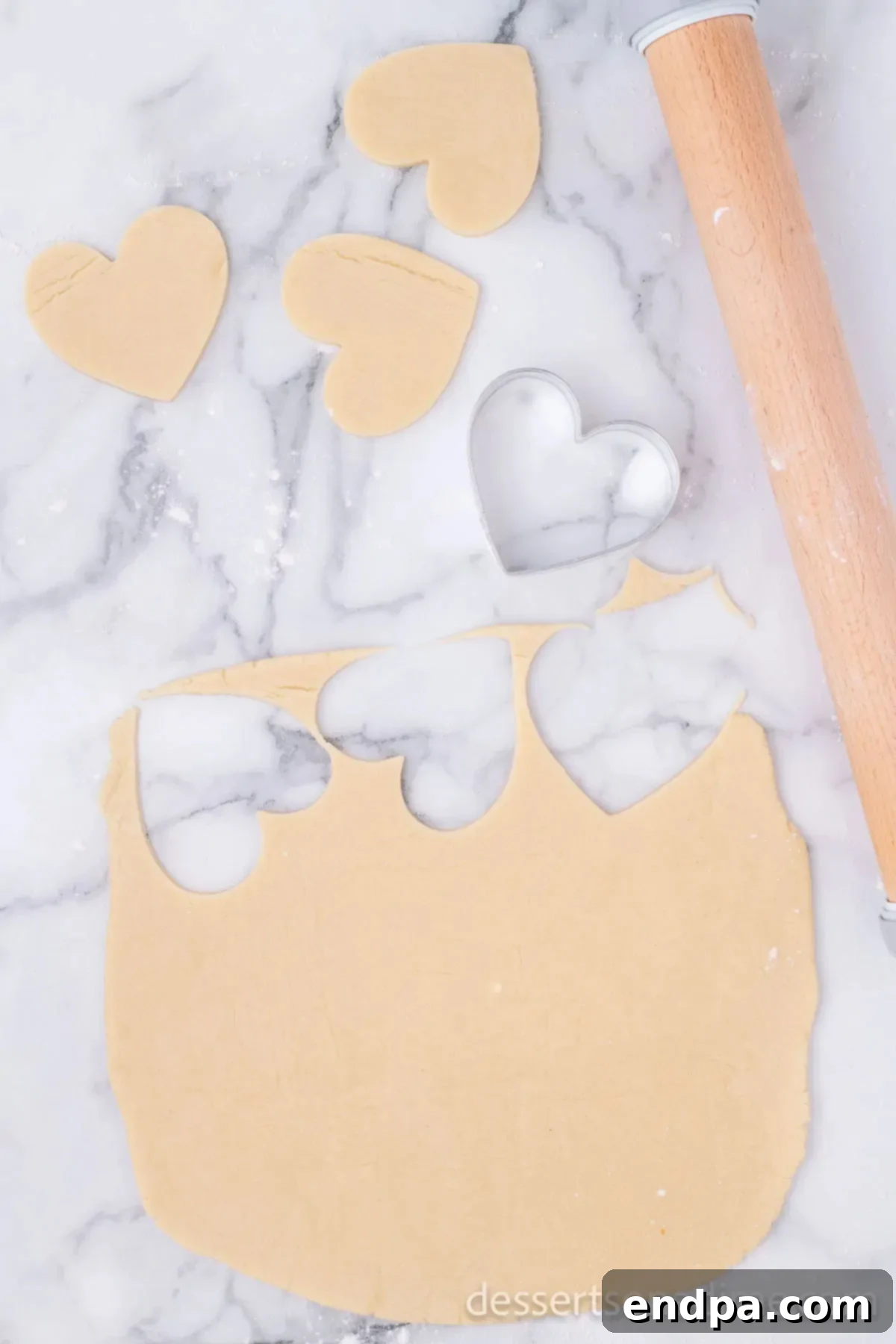 Rolled out cookie dough on a floured surface with heart-shaped cookie cutters in use, cutting out individual cookies.