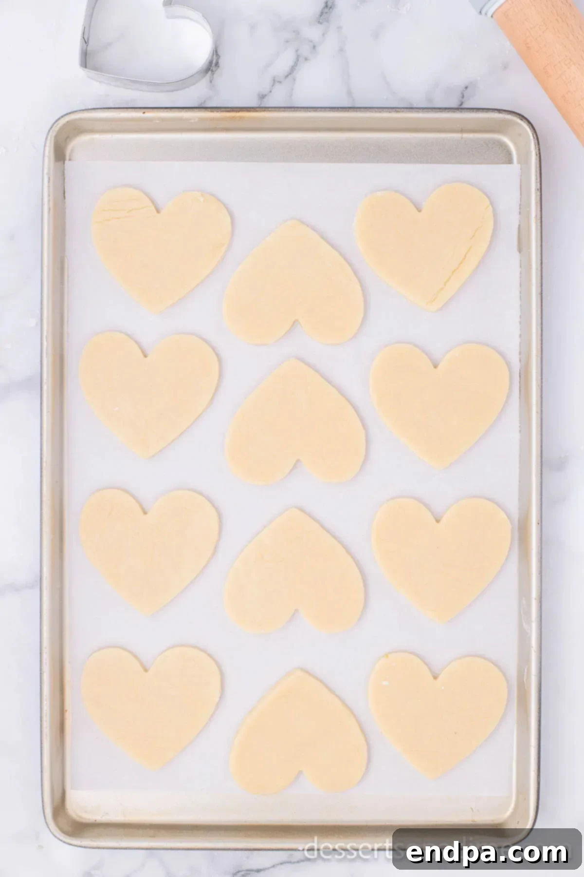 Unbaked heart-shaped cookies neatly arranged on a baking sheet lined with parchment paper.