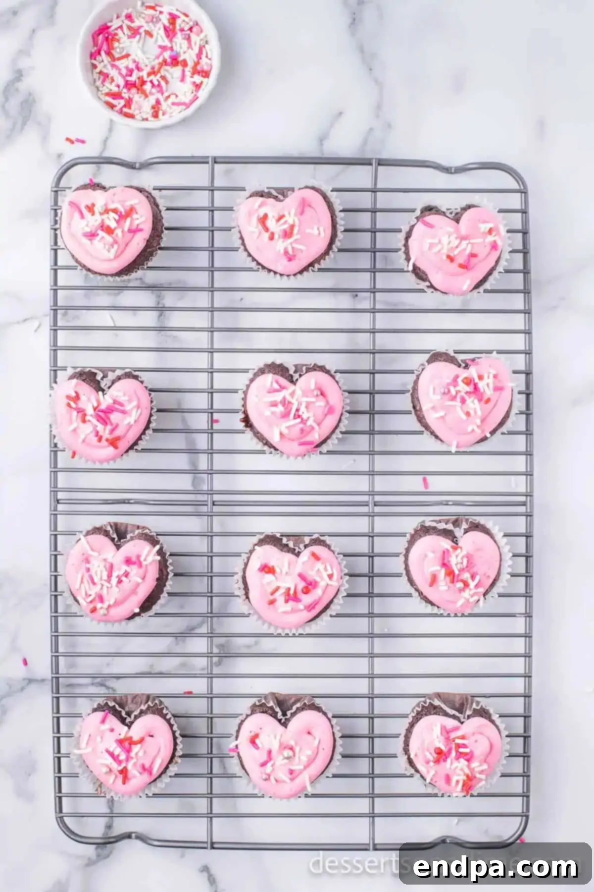 Cupid's Cupcakes 11 Festive sprinkles being added to the frosted heart-shaped cupcakes.