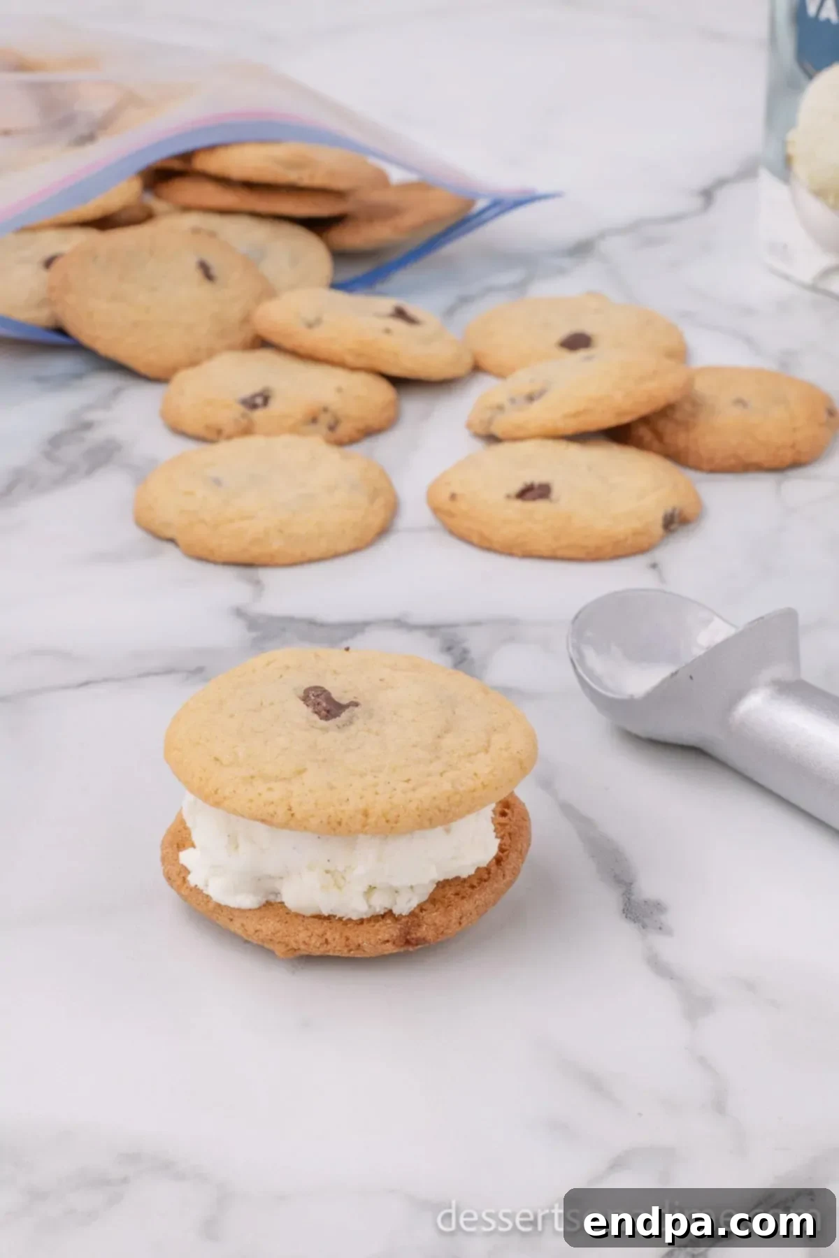 A second chocolate chip cookie being gently placed on top of the ice cream scoop, completing the Chipwich sandwich.