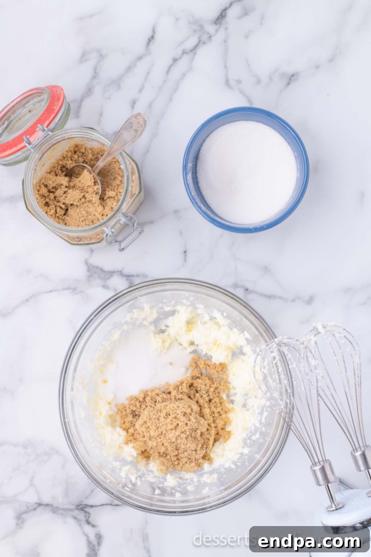Creamy mixture of butter, granulated sugar, and brown sugar after being blended in a mixing bowl, showcasing a light and fluffy texture.