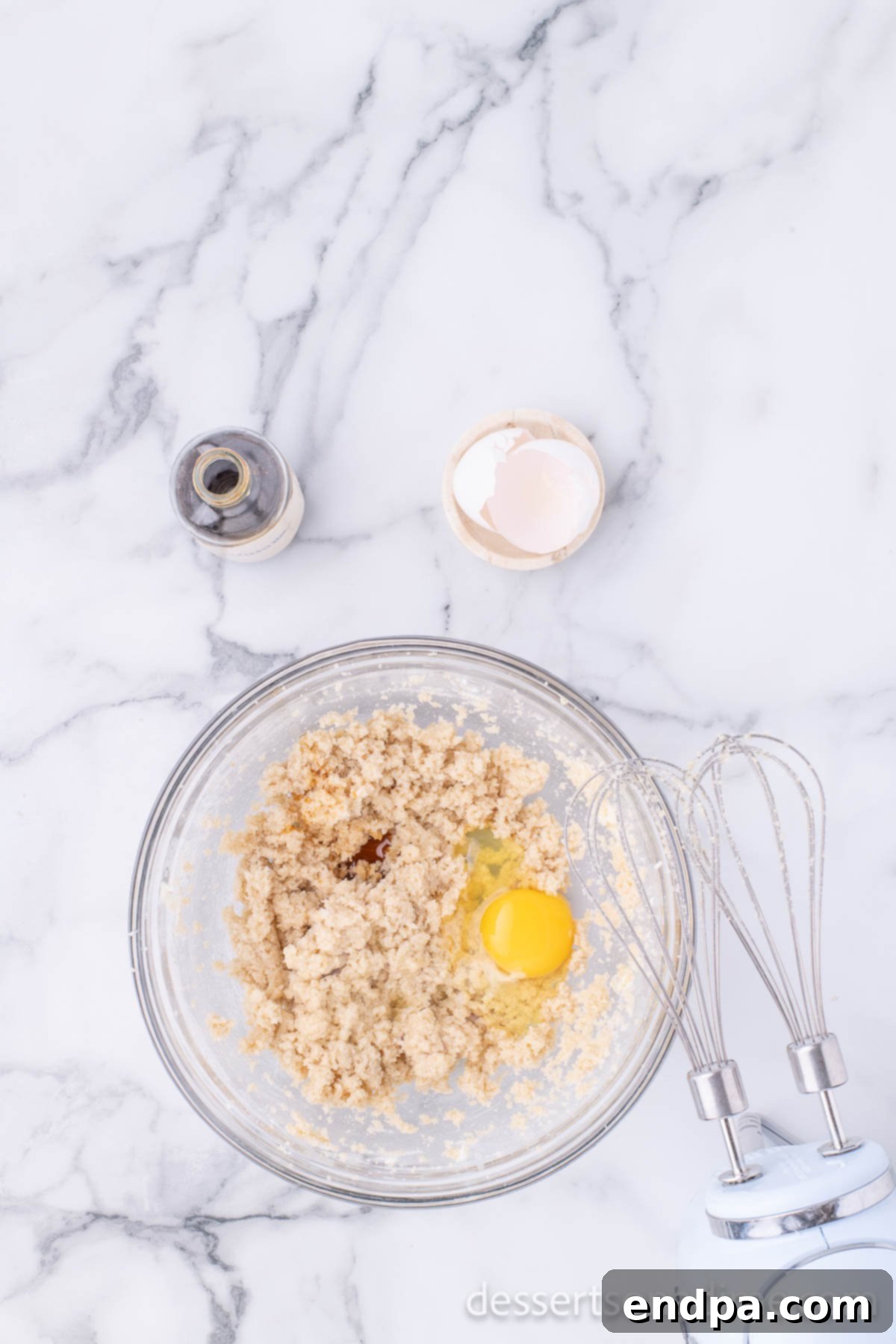 An egg being cracked and added to the creamy butter and sugar mixture in a large mixing bowl, ready for further blending.