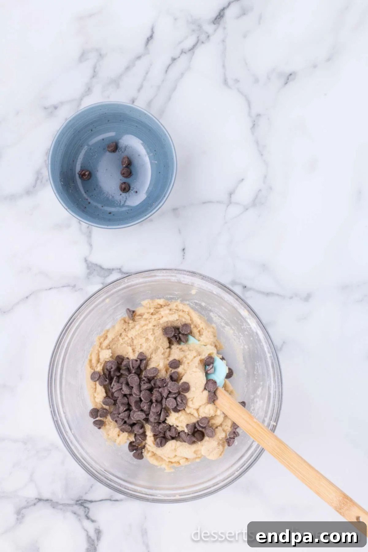 Semi-sweet chocolate chips being gently folded into the cookie dough mixture by hand, ensuring even distribution.