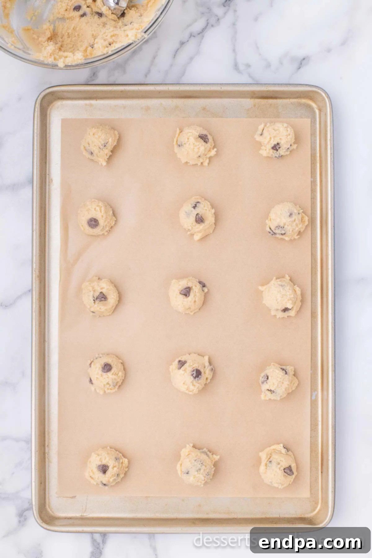 Balls of chocolate chip cookie dough evenly spaced on a parchment-lined baking sheet, ready for the oven.