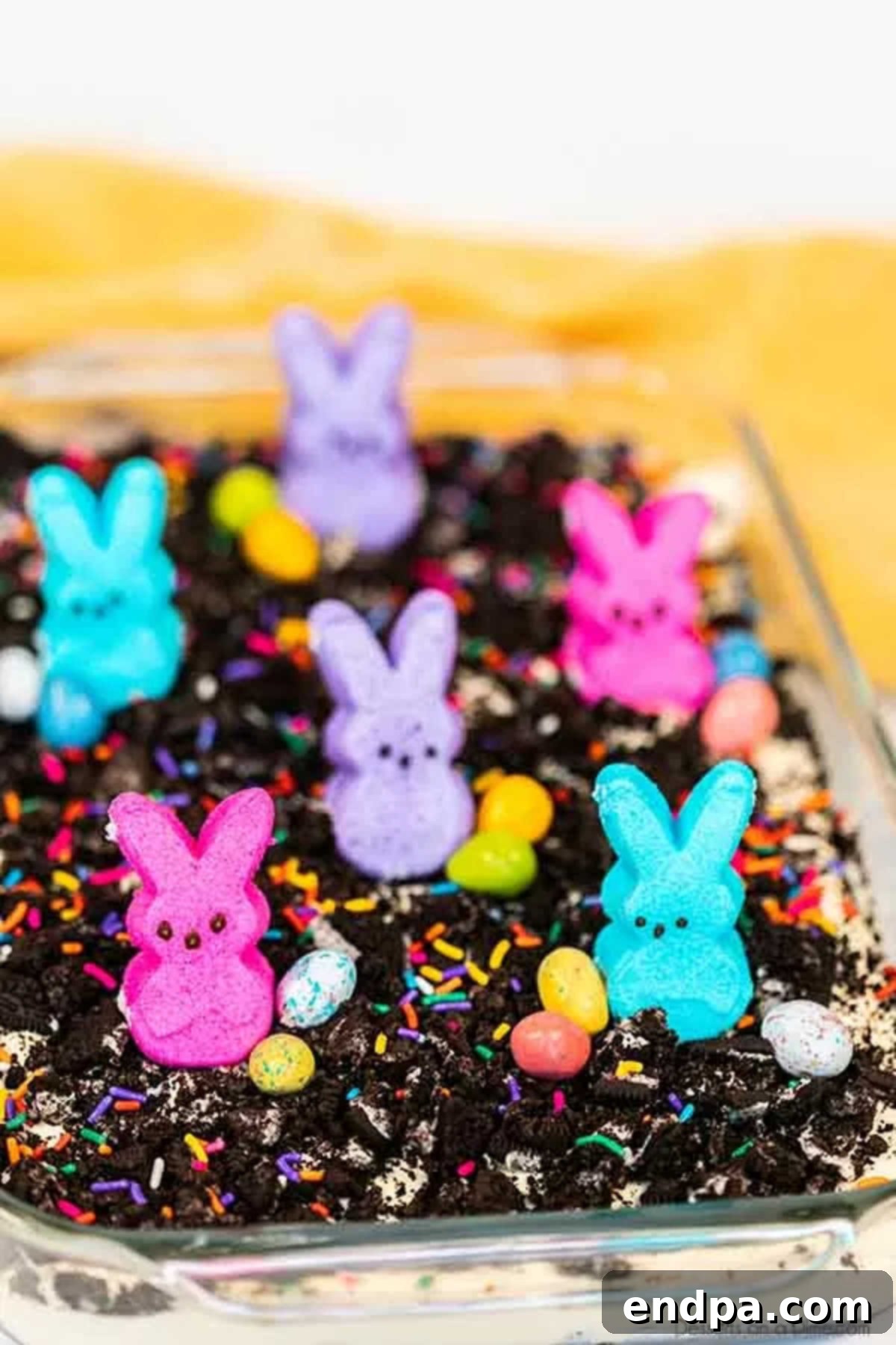 Easter dirt cake is an easy and delicious no bake treat perfect for dessert on Easter. This fun dessert is decorated with Easter peeps, candy and more. Easter dirt cake in baking dish, adorned with colorful Easter candies and Peeps.