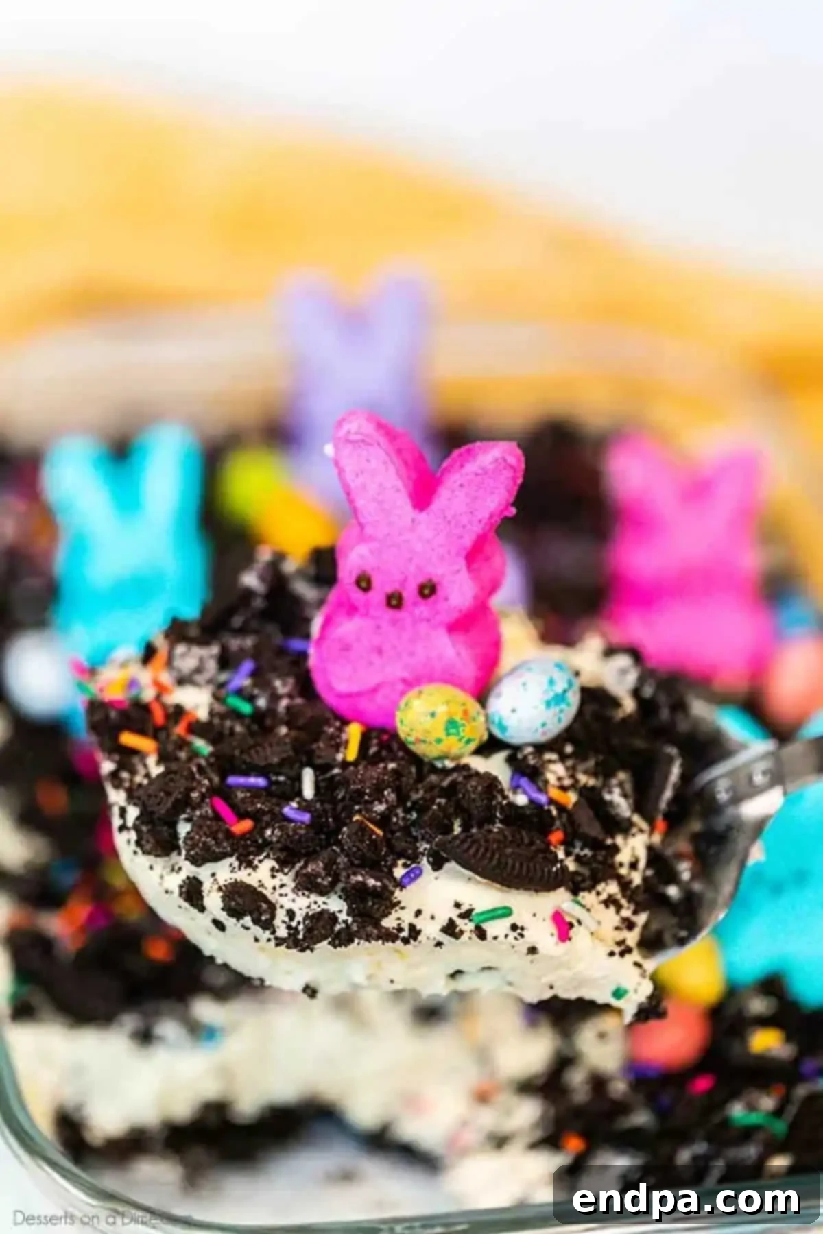 Easter dirt cake is an easy and delicious no bake treat perfect for dessert on Easter. This fun dessert is decorated with Easter peeps, candy and more. A scoop of Easter dirt cake being served from the baking dish, revealing its creamy layers and cookie crumbs.