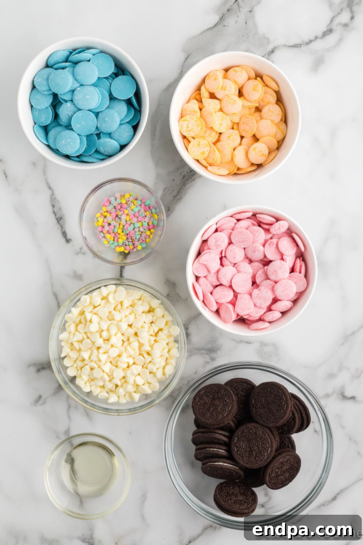 A flat lay showing all ingredients for Easter Oreos: Oreo cookies, white chocolate chips, pink, blue, and yellow candy melts, and a bottle of vegetable oil.