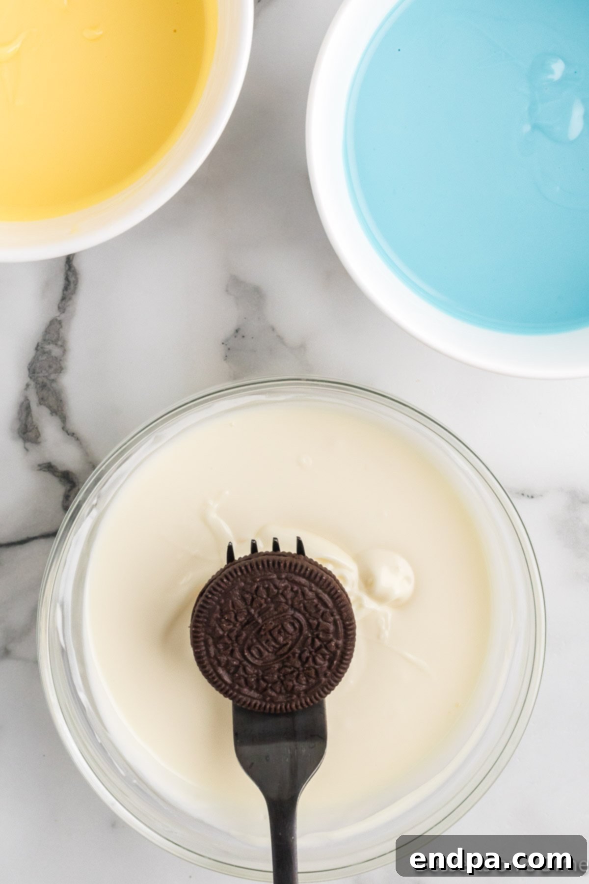 An Oreo cookie being dipped into a bowl of melted white chocolate using a fork.