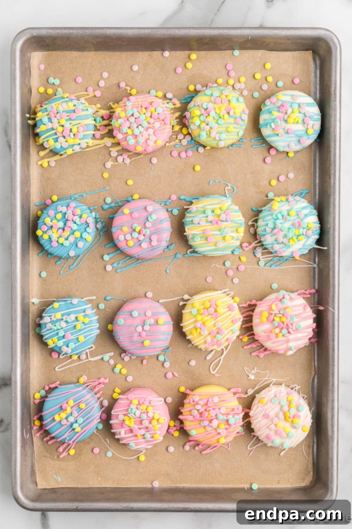 Decorated Oreo cookies with drizzles and sprinkles on a cookie sheet, ready for final setting.