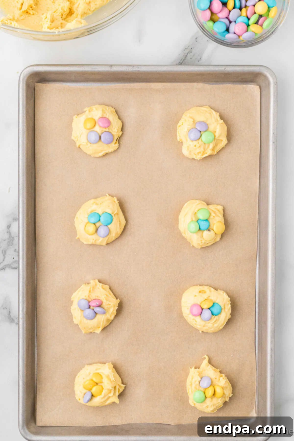 Cookie dough balls on a baking sheet with pastel M&M's pressed onto the tops.
