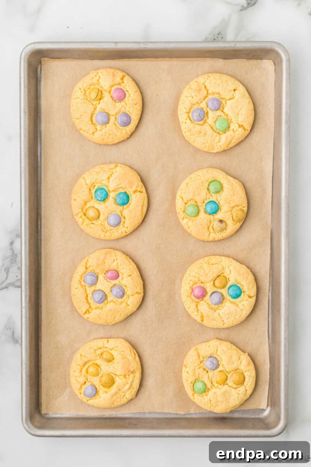 Freshly baked cookies cooling on a baking sheet, with additional M&M's pressed onto them.