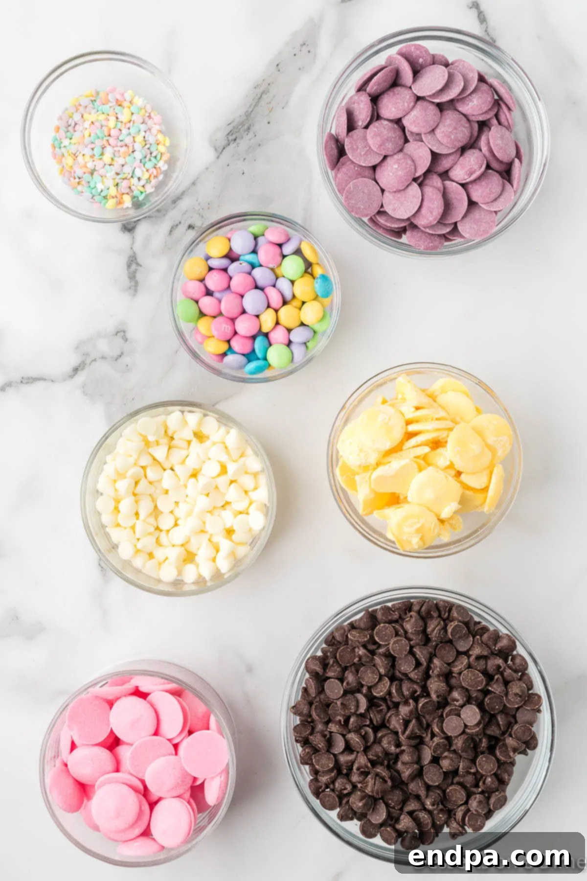 Ingredients for Easter chocolate bark laid out: chocolate chips, white chocolate chips, pink, purple, and yellow candy melts, pastel M&Ms, and pastel sprinkles.