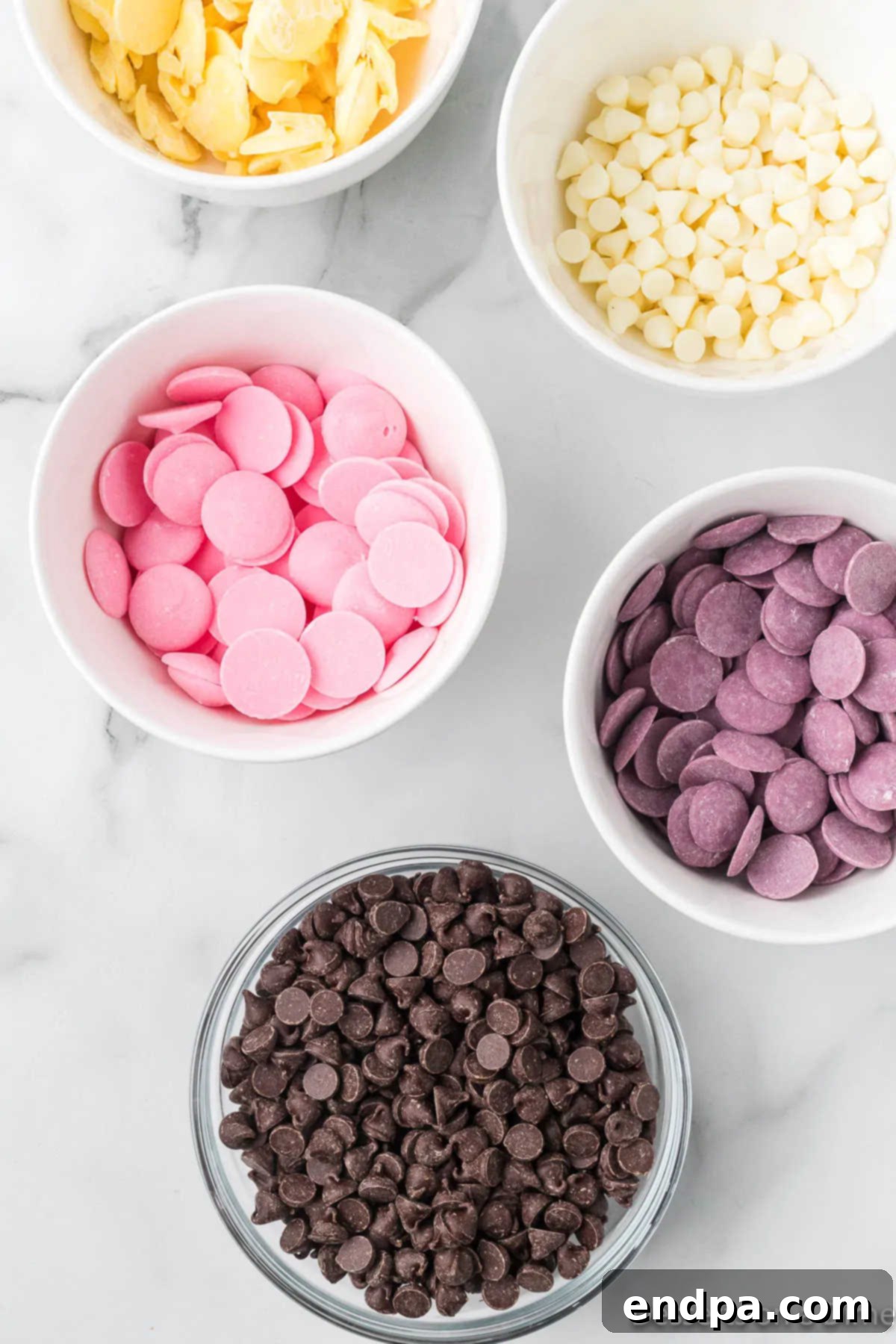 Bowls filled with chocolate chips and various colored candy melts, ready for melting.