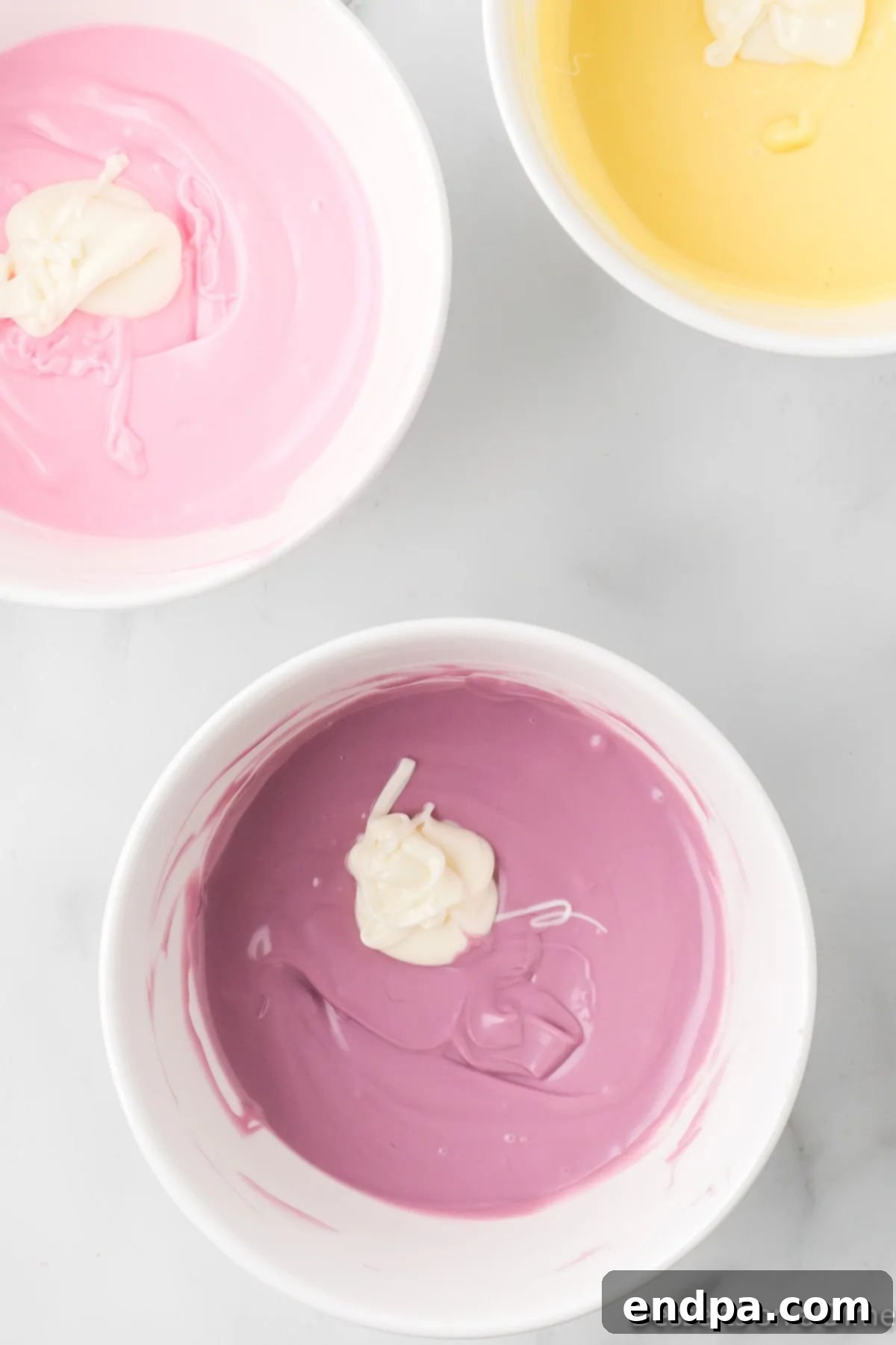 Melted white chocolate being stirred into a bowl of colored candy melts to create a pastel shade.
