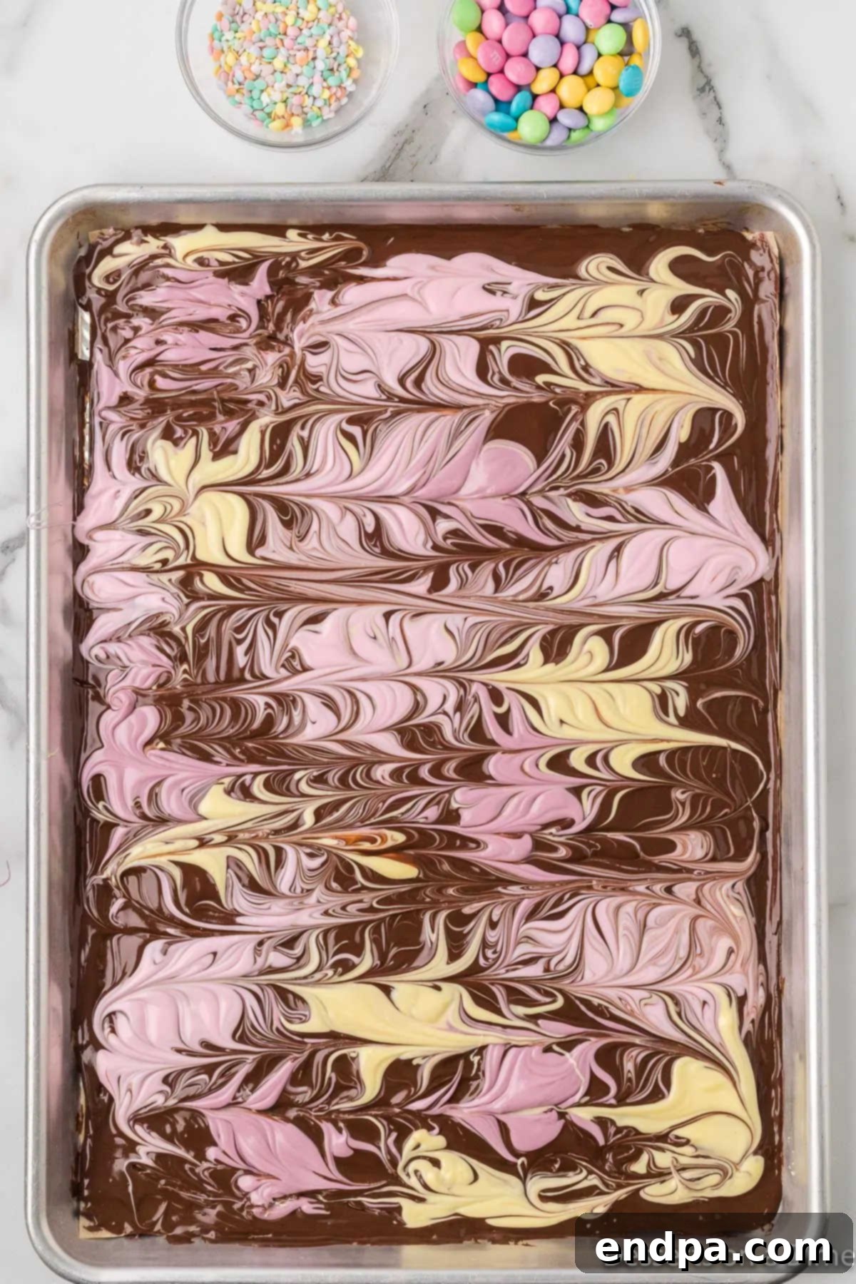 A butter knife tip swirling the colored candy melts into the dark chocolate base to create a marbled effect.