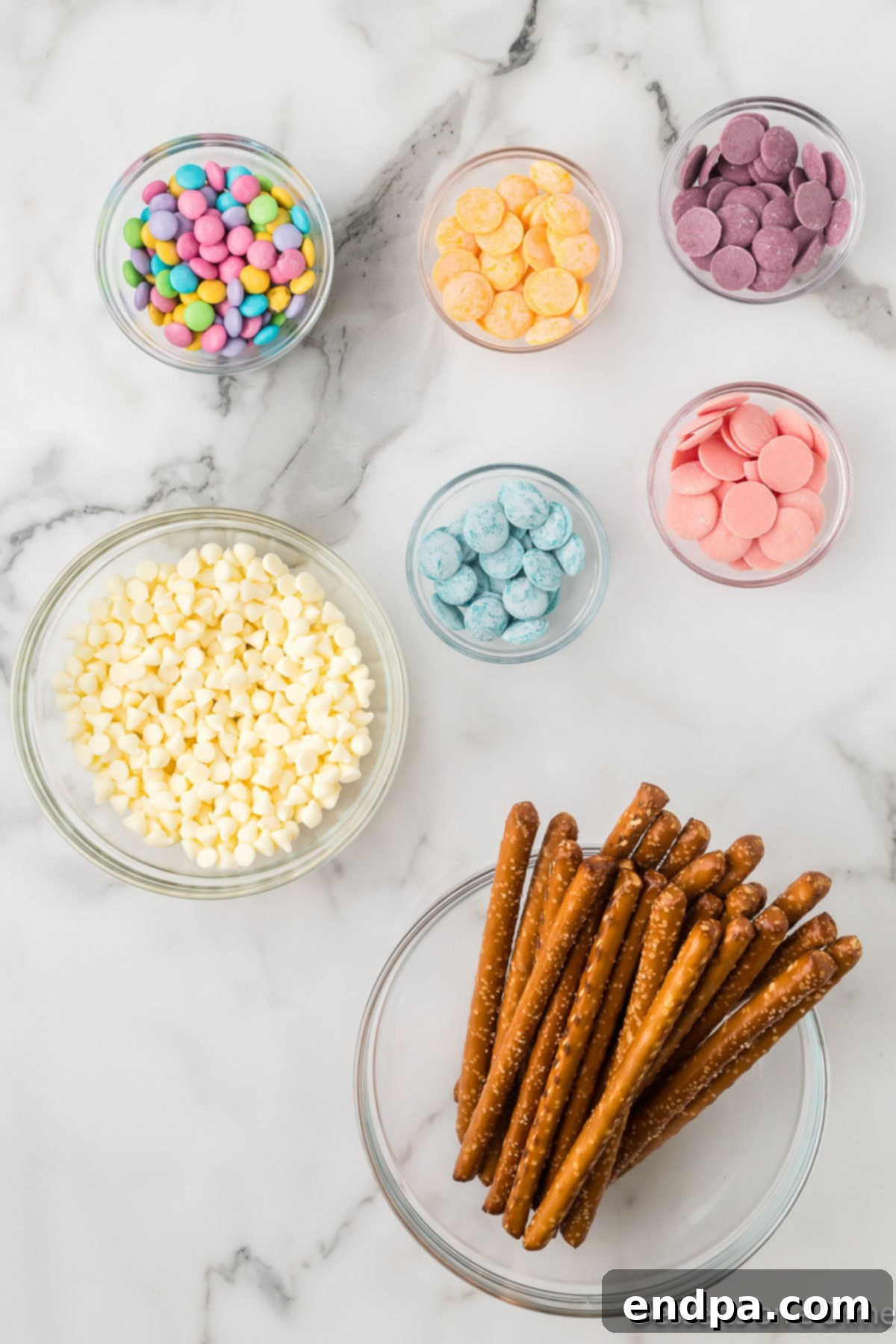 Ingredients for recipe - pretzel rods, white chocolate chips, candy melts and pastel m&ms. 