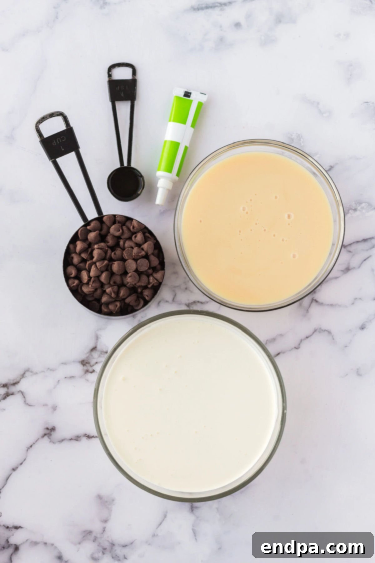 Ingredients for recipe: chocolate chips, heavy cream, sweetened condensed milk, vanilla, green food coloring laid out on a surface.