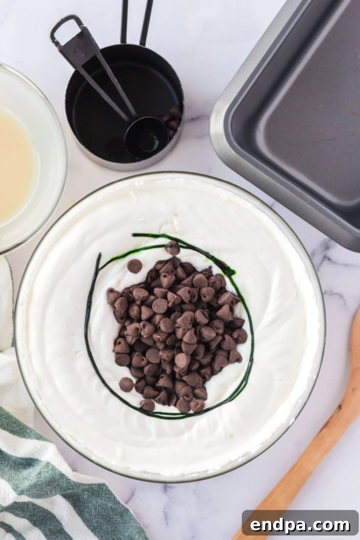 Chocolate chips folded into mint ice cream mixture in a bowl.