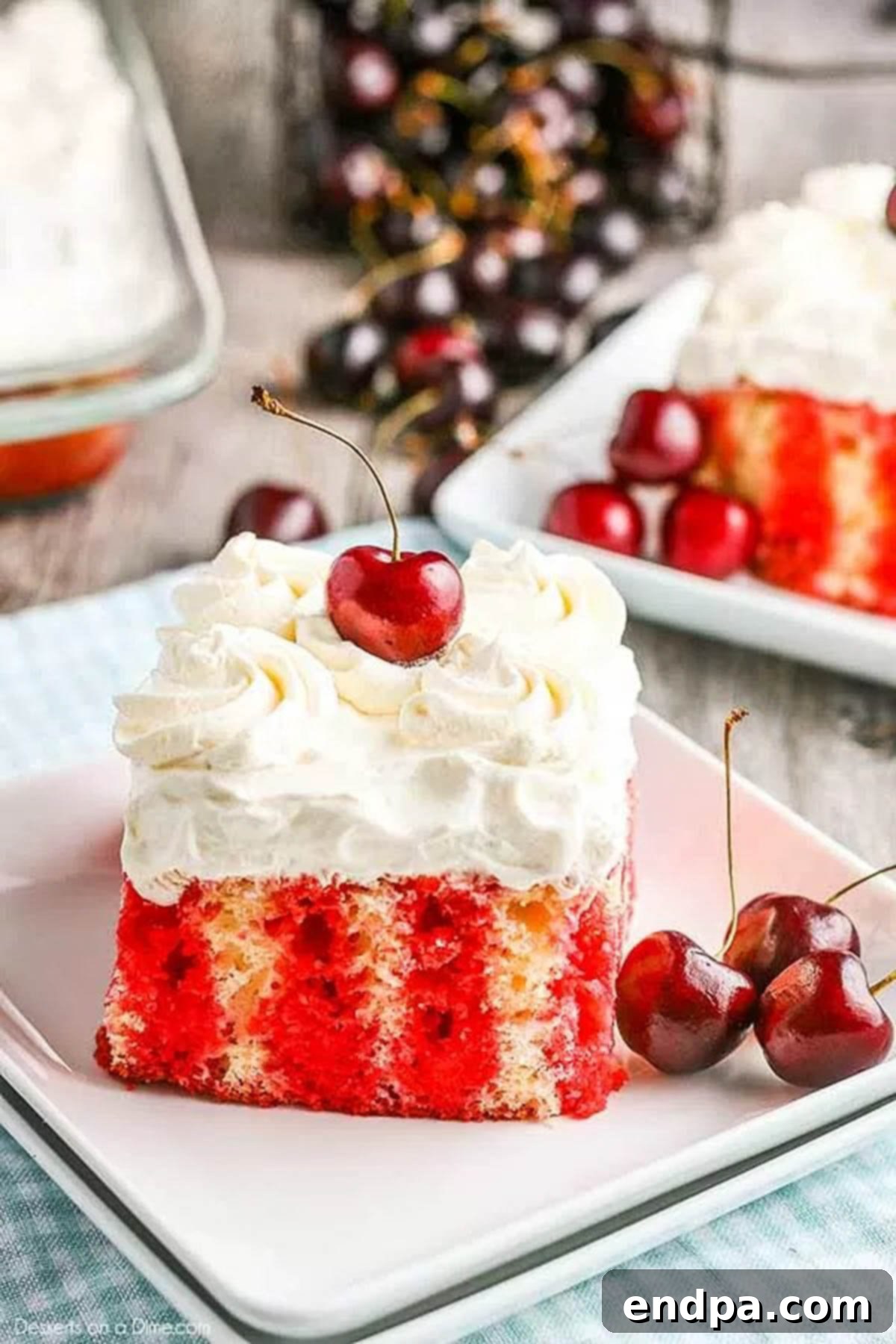 A slice of Cherry Poke Cake on a white plate, garnished with fresh cherries.