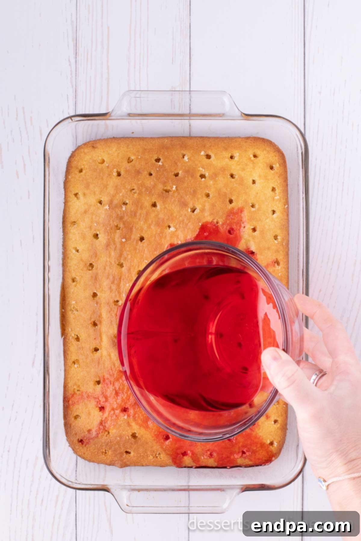 Cherry jello being poured over the poked cake.