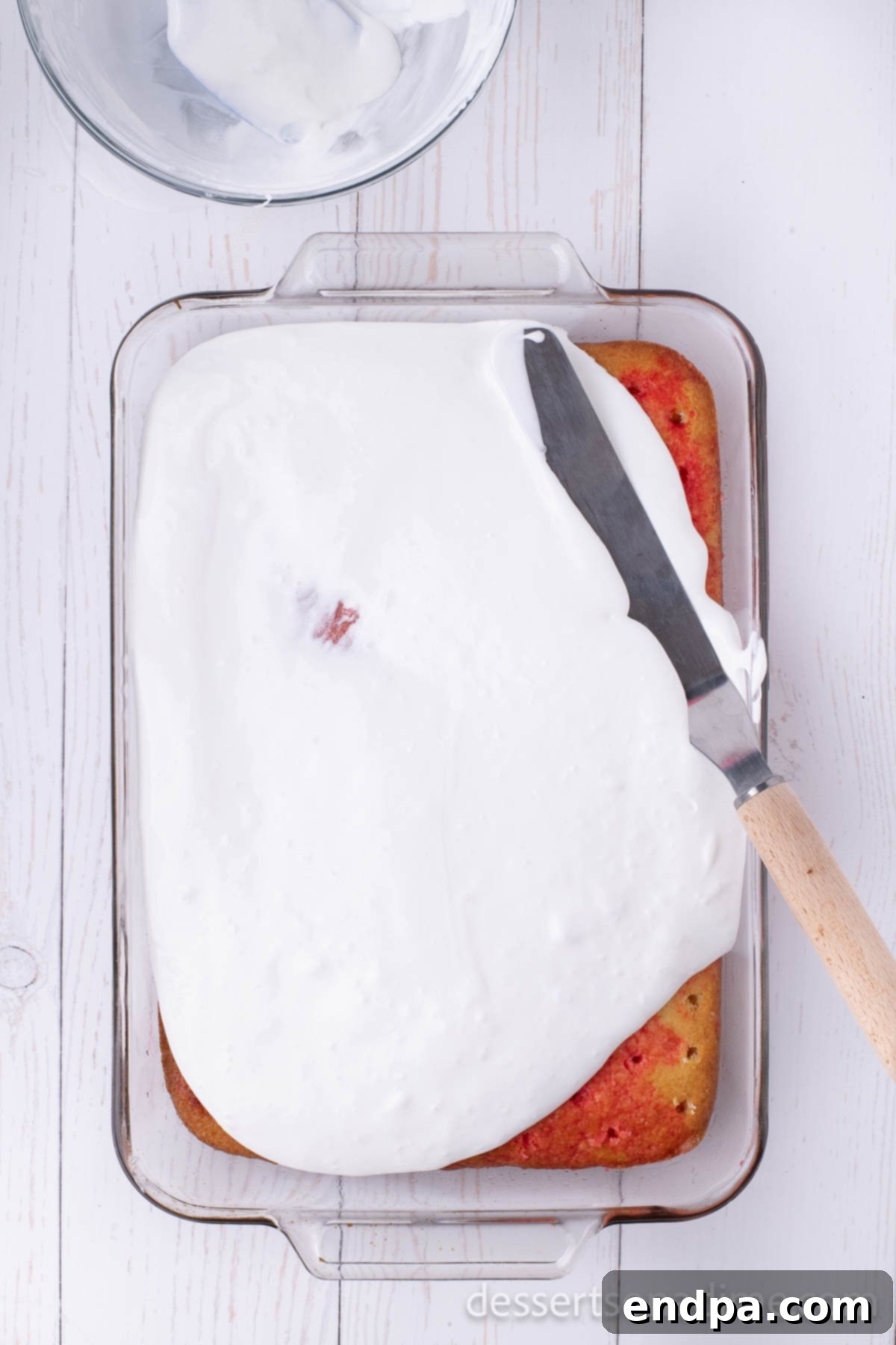 Frosting being spread over the chilled cherry poke cake.
