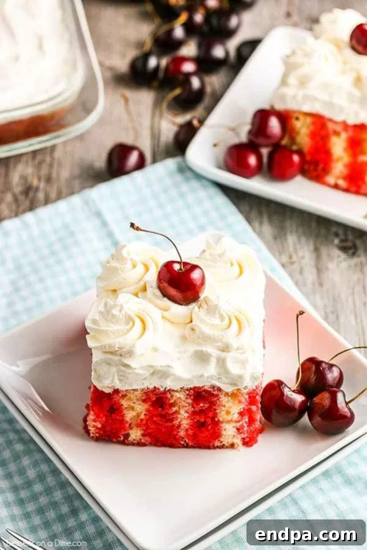 Two slices of Cherry Poke Cake on a white plate, with fresh cherries beside them.