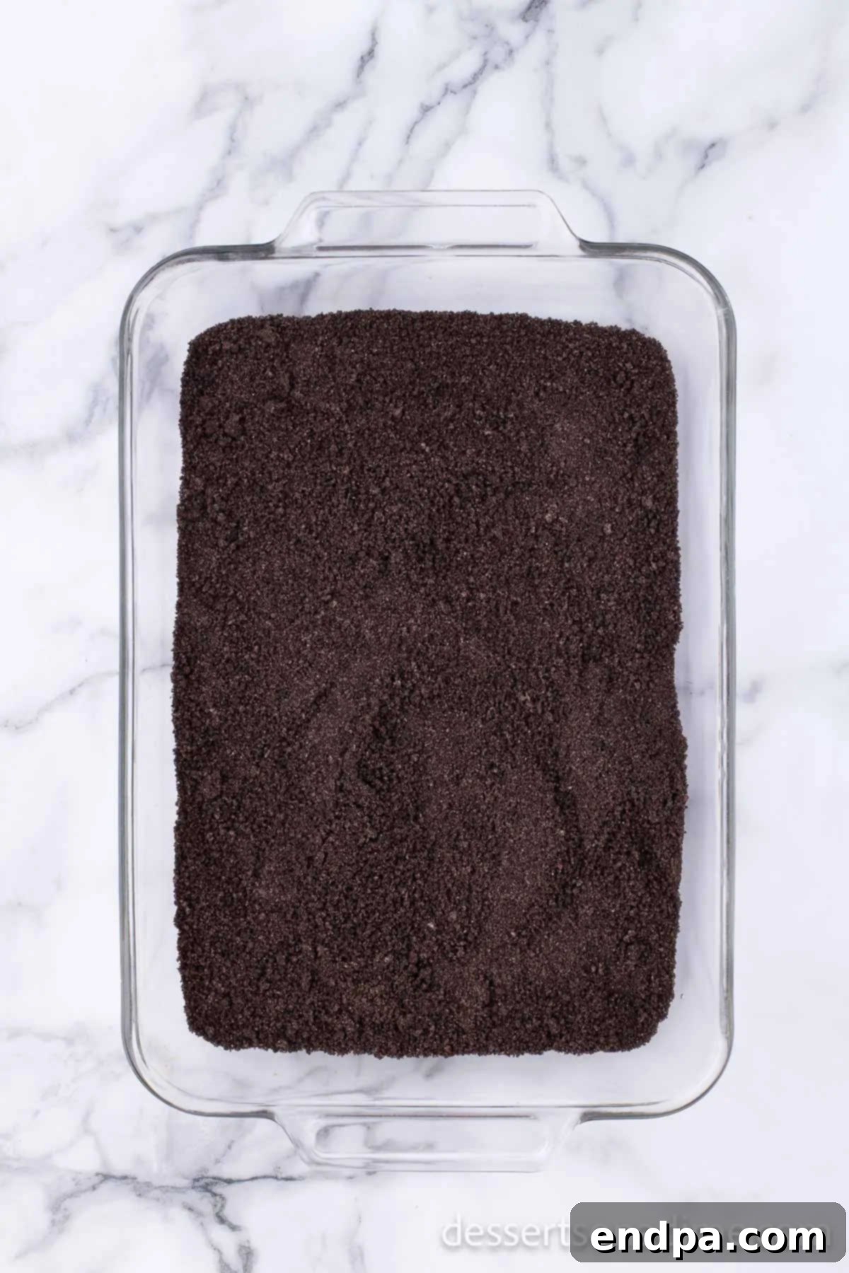 Crushed Oreo cookie crumbs forming the base layer in a 9x13 inch baking dish.