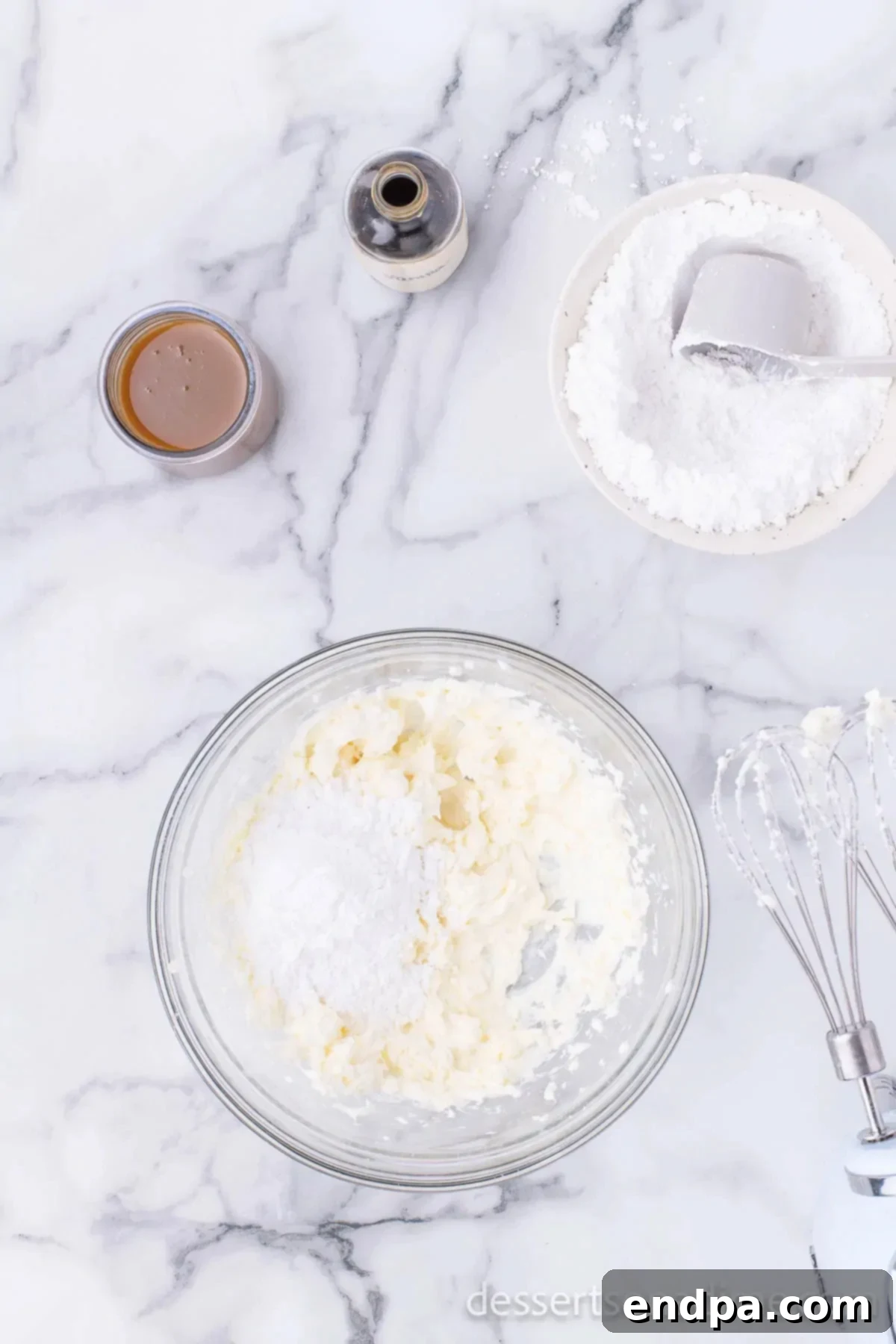 Cream cheese and powdered sugar being beaten together in a large mixing bowl with a hand mixer.