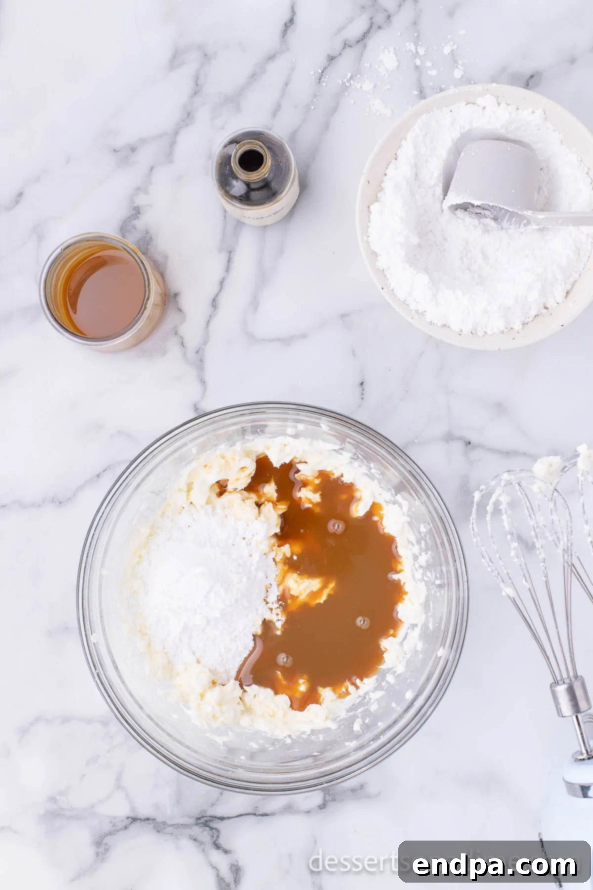 Salted caramel sauce and vanilla extract being added to the cream cheese and sugar mixture in a bowl.