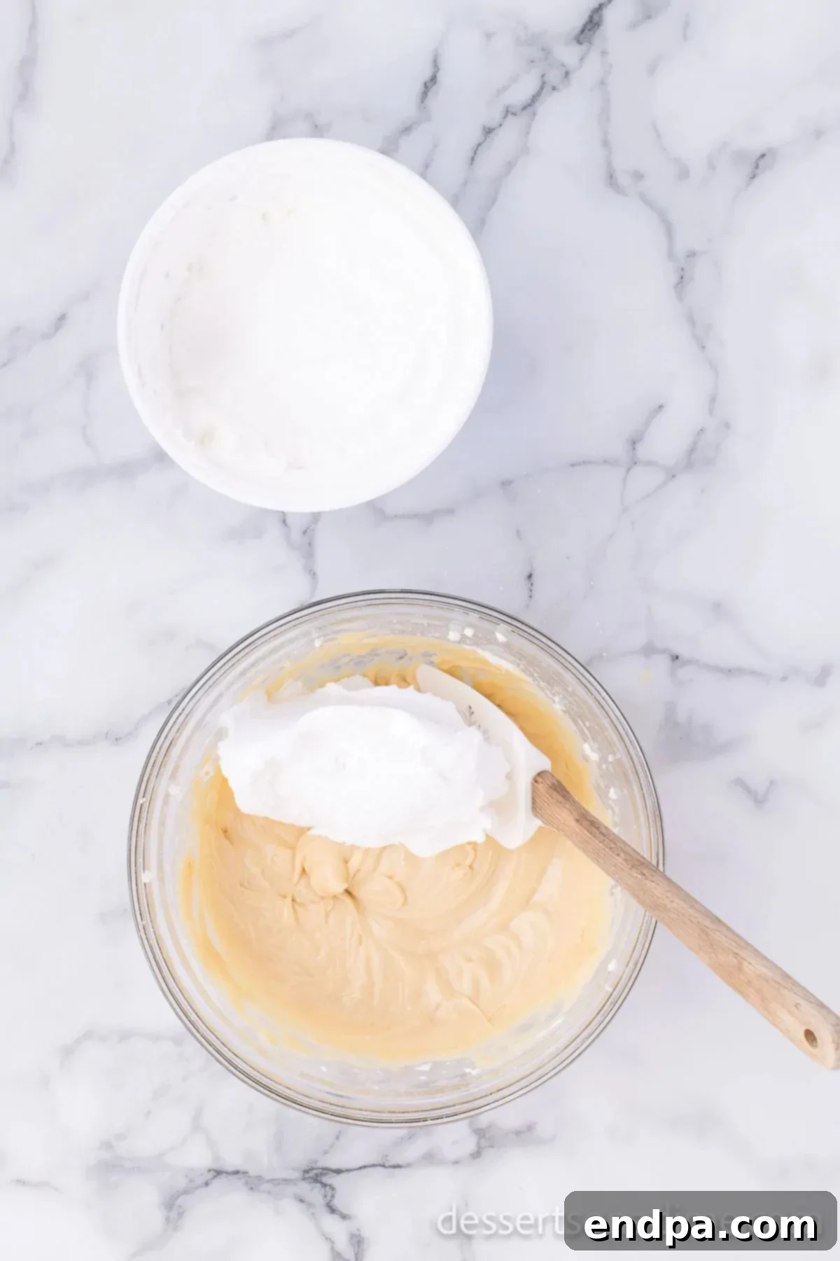 Half of the whipped topping being folded gently into the cream cheese and caramel mixture in a bowl.