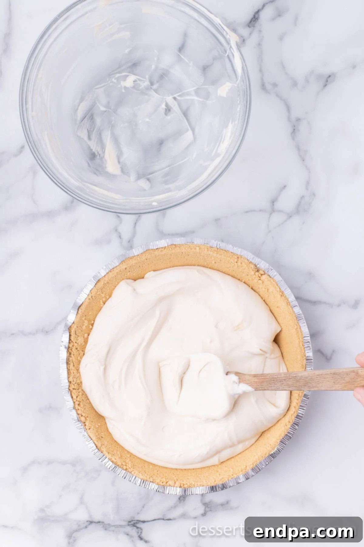 The finished pie filling being spread evenly into a pre-made graham cracker crust in a pie pan.