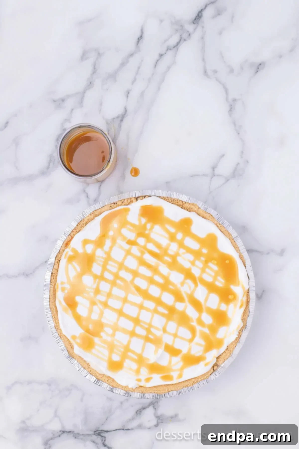 Salted caramel sauce being artfully drizzled over the whipped topping of the finished no-bake pie.