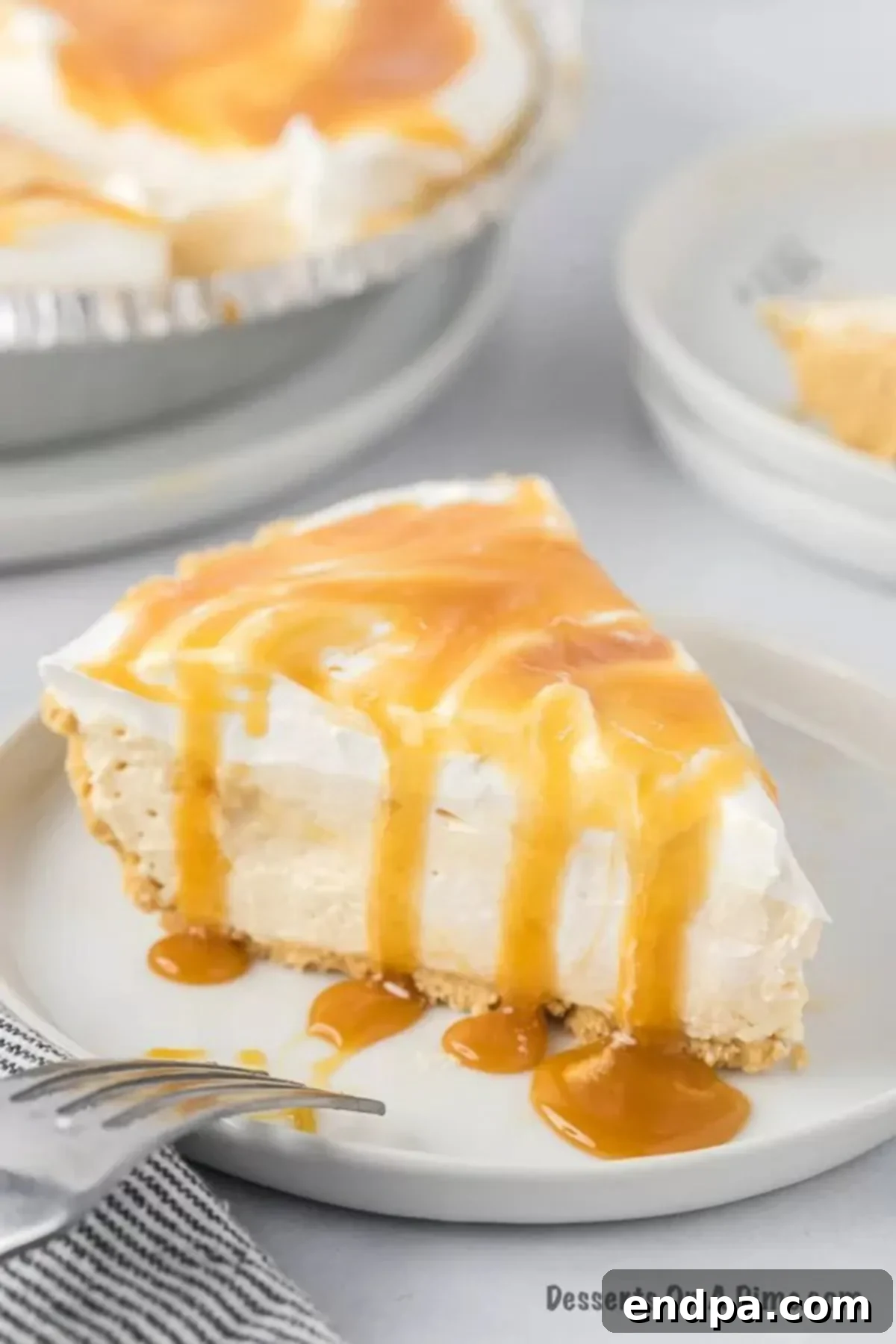 A beautiful slice of no-bake salted caramel pie, showing its layers, resting on a white plate with a fork.