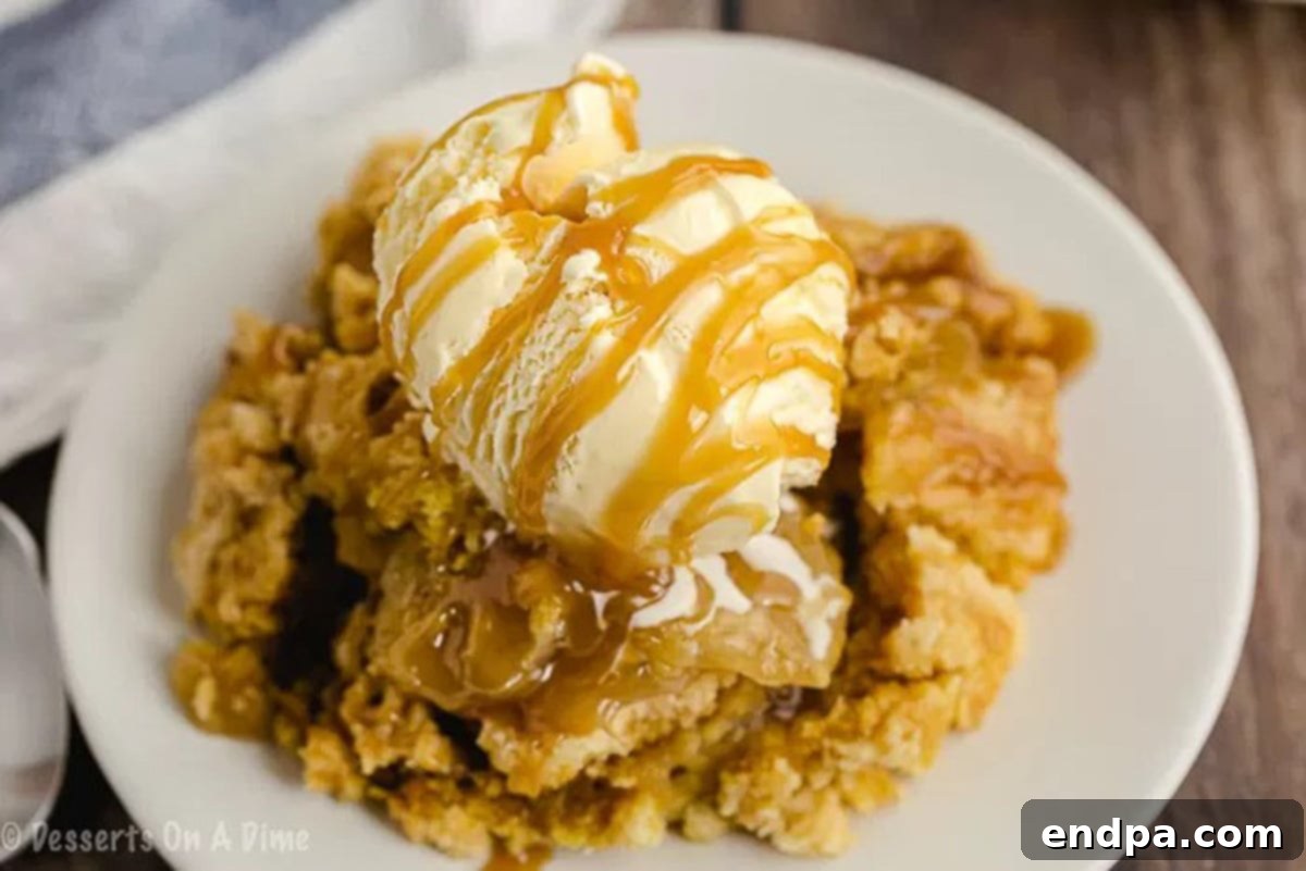 Close up image of warm caramel apple dump cake on a white plate, generously topped with a scoop of vanilla ice cream and a luscious caramel sauce drizzle.