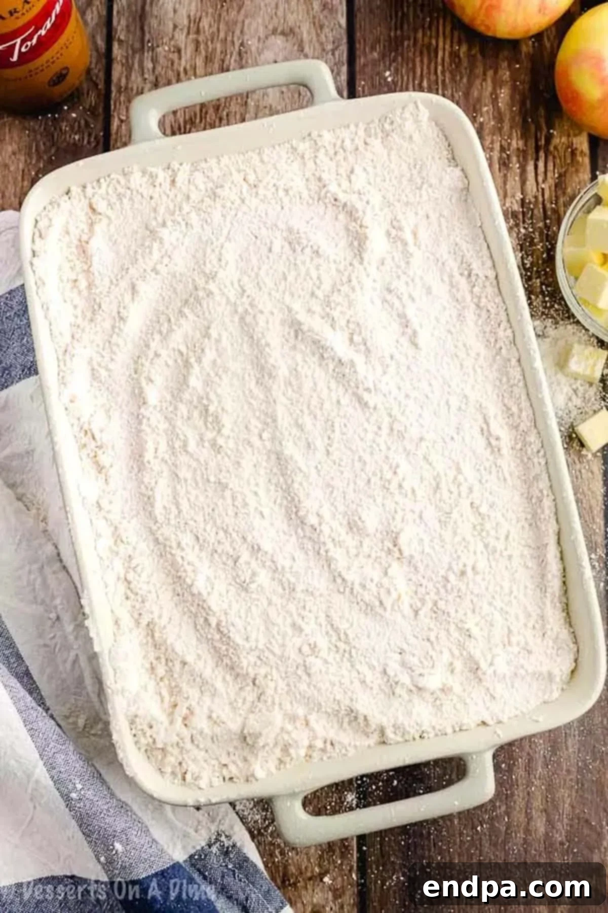 Dry yellow cake mix sprinkled over the caramel and apple layers, ready for butter.